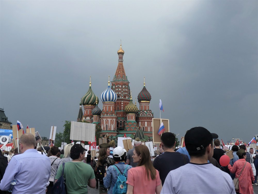  Before the Immortal Regiment and under dark clouds, Saint Basil’s Cathedral emerges. 