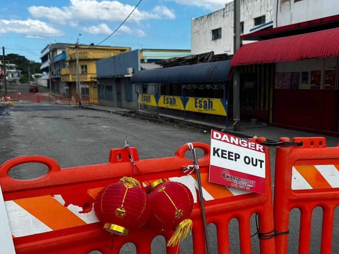   Photo 2 : A construction barricade, adorned by Lunar New Year lanterns, cordons off a city block that remains structurally unsound following the earthquake—a testament to both the barricade’s longevity but also Port Vila’s resilience and joy in adv