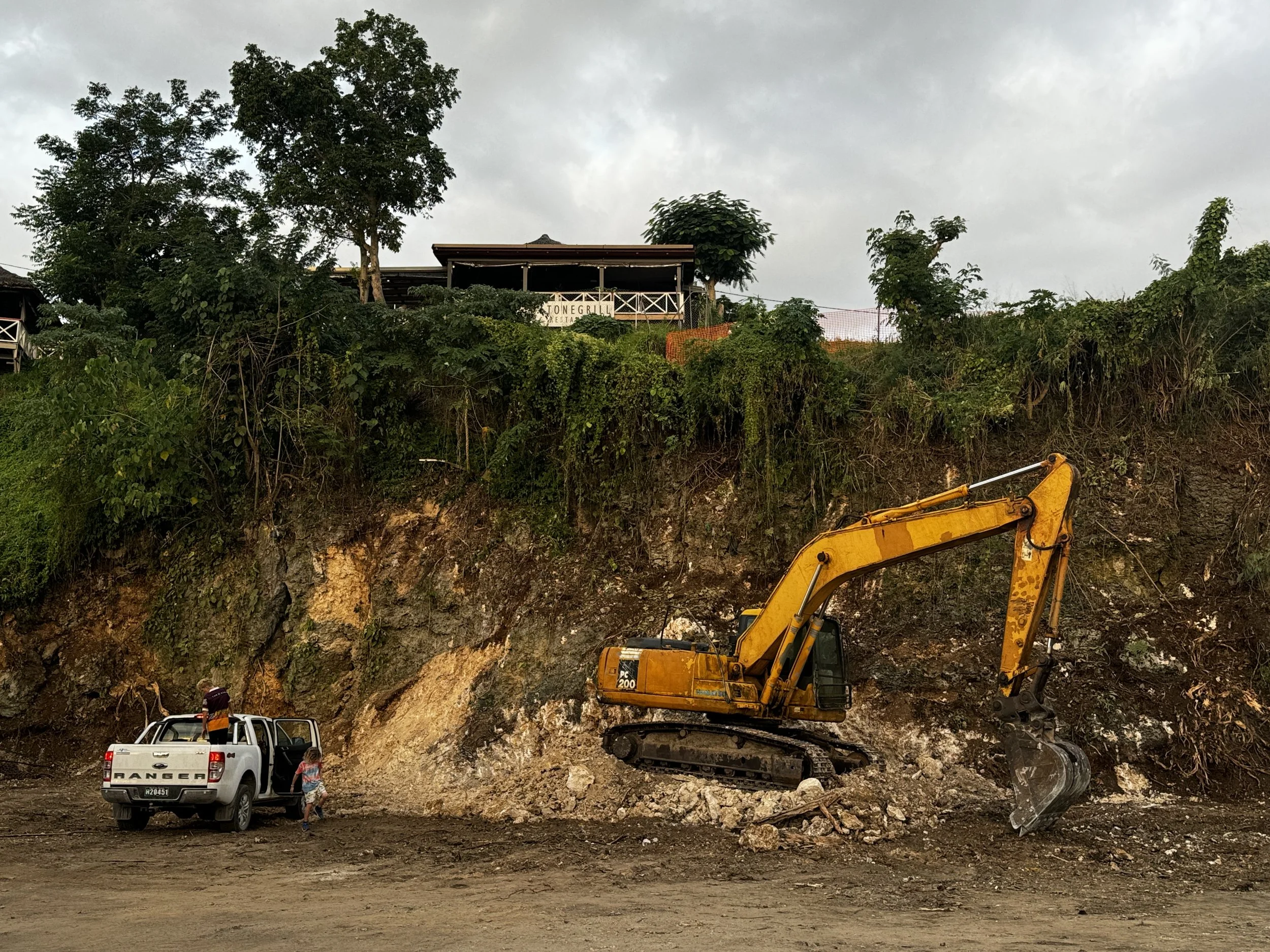   Photo 10:  Two children exit a truck beneath a tall excavator—everyday life unfolding in the shadow of reconstruction. 