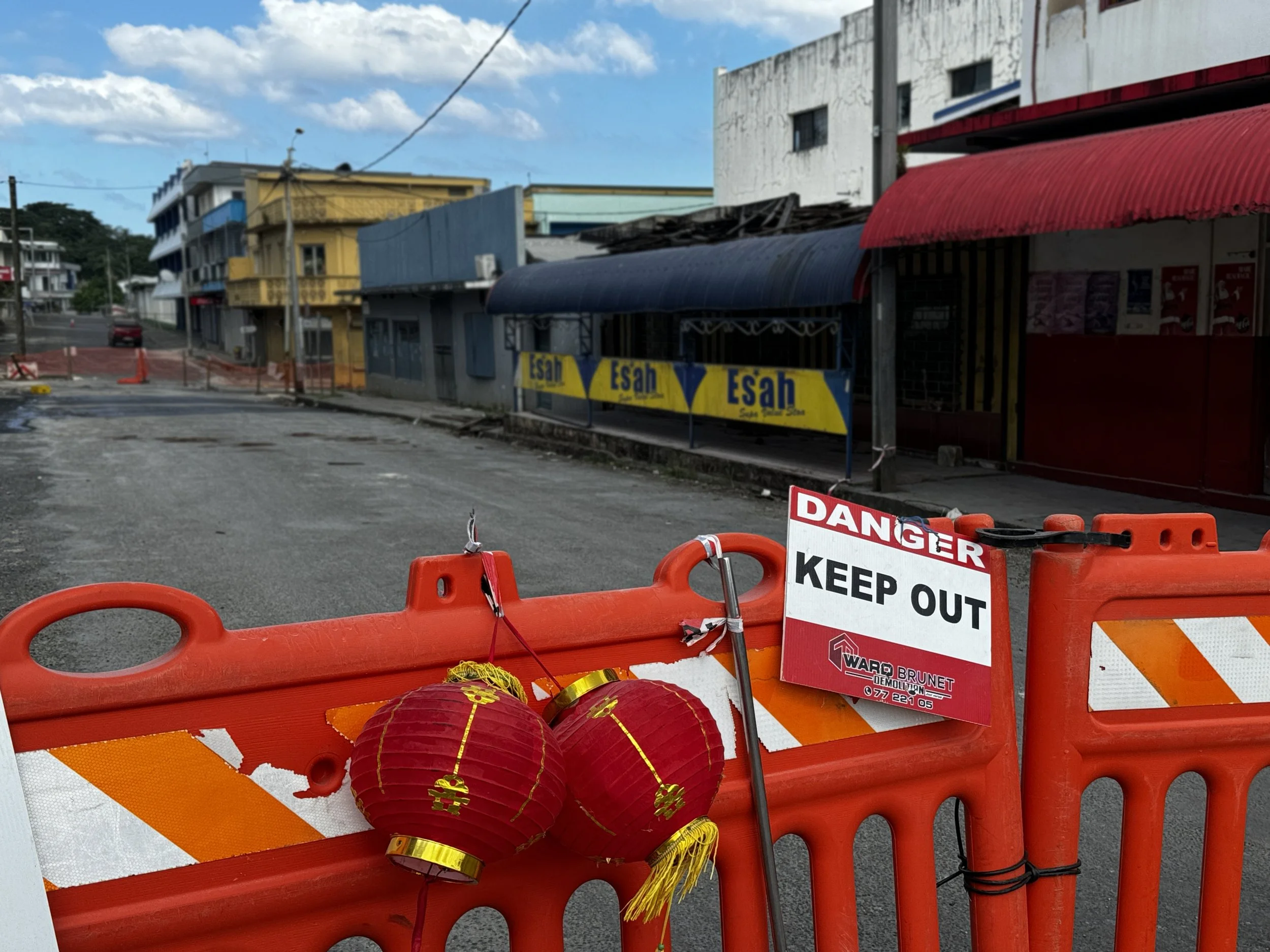   Photo 2 : A construction barricade, adorned by Lunar New Year lanterns, cordons off a city block that remains structurally unsound following the earthquake—a testament to both the barricade’s longevity but also Port Vila’s resilience and joy in adv