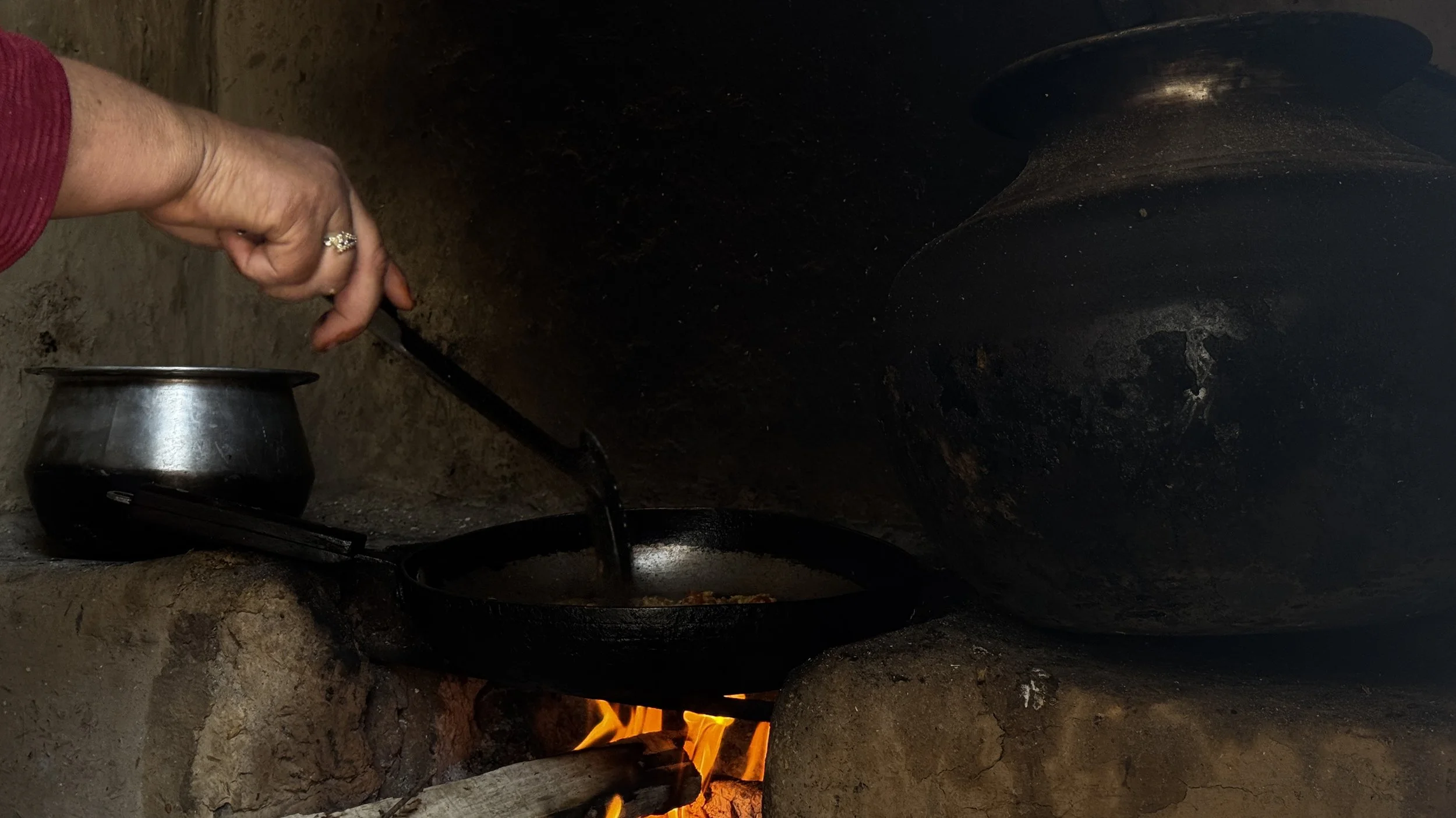   Photo 3:  A woman prepares a meal over a woodfire inside her home in rural Pakistan. Domestic spaces such as these reflect the often unseen labor of women, whose daily contributions sustain families amid prolonged displacement. 