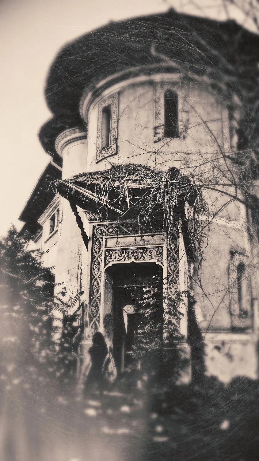 A vintage black-and-white photograph of a Victorian-style house with ornate trim and a rounded turret. There are leafless trees and a person standing near the doorway. putrid space © Alexandra Crisbășan