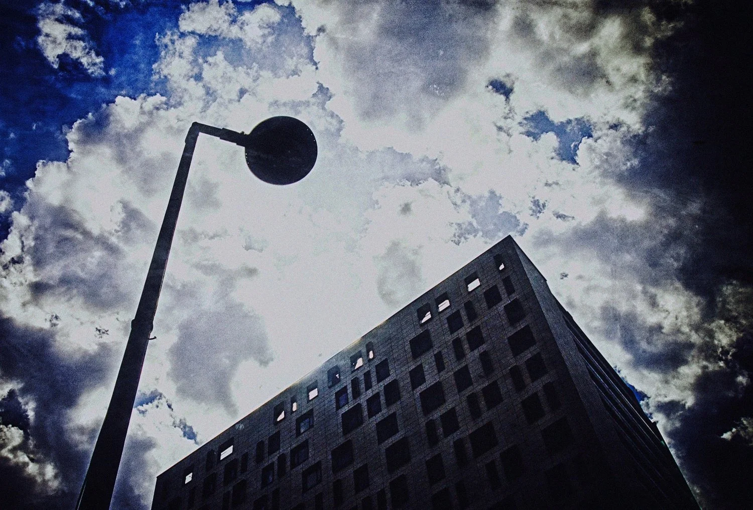 A tall street lamp next to a high-rise building under a cloudy sky. putrid space © Alexandra Crisbășan