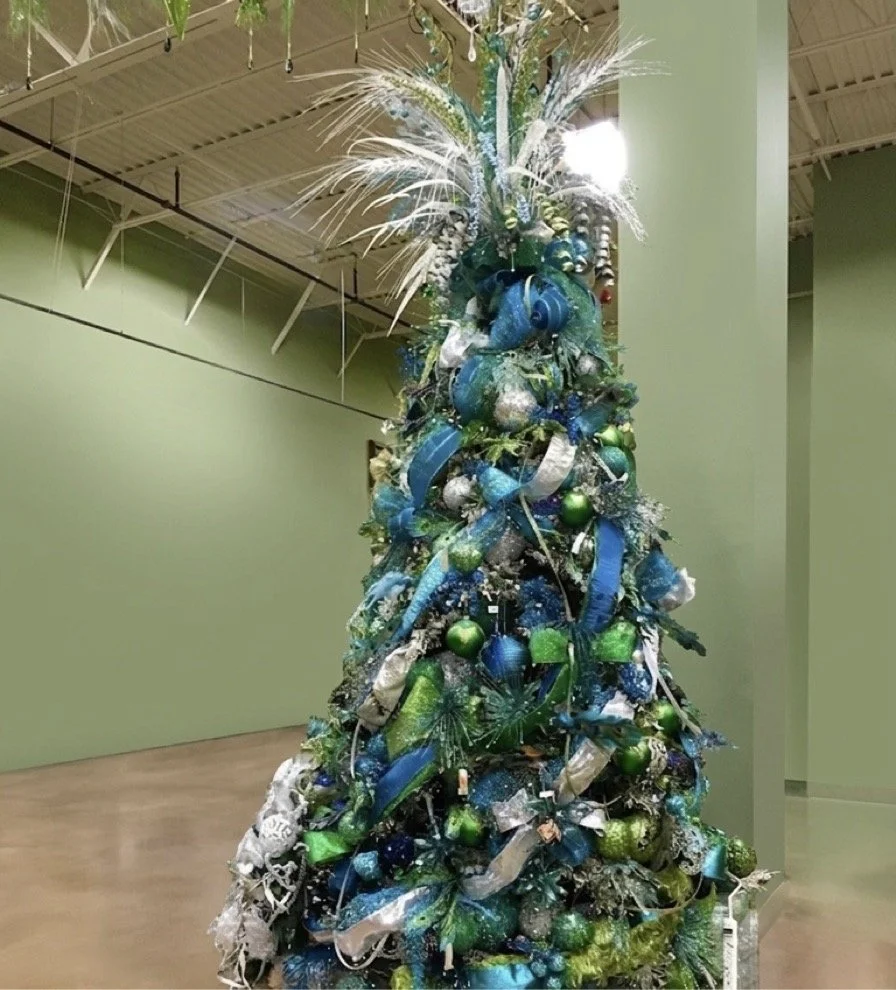 Peacock-themed Christmas tree in iridescent teal, blue, and green with wide ribbon, glass ornaments, and white feather plumes
