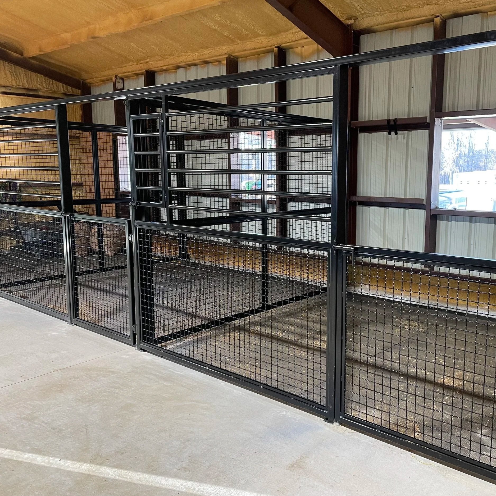 Black metal livestock cage with wire mesh panels inside a wooden structure with metal siding, unfinished ceiling, and concrete floor