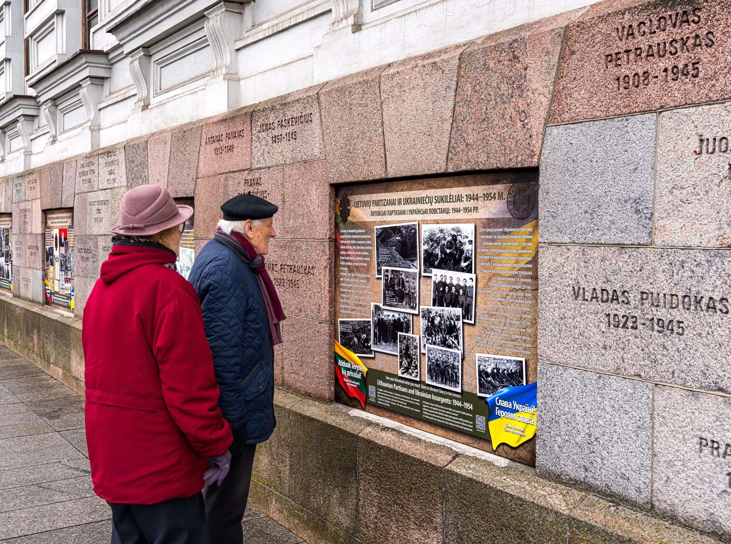 Vilnius. At the KGB’s haunted walls, survivors of fear read words with Ukraine flag, where memory warns: oppression returns when silence replaces resistance.