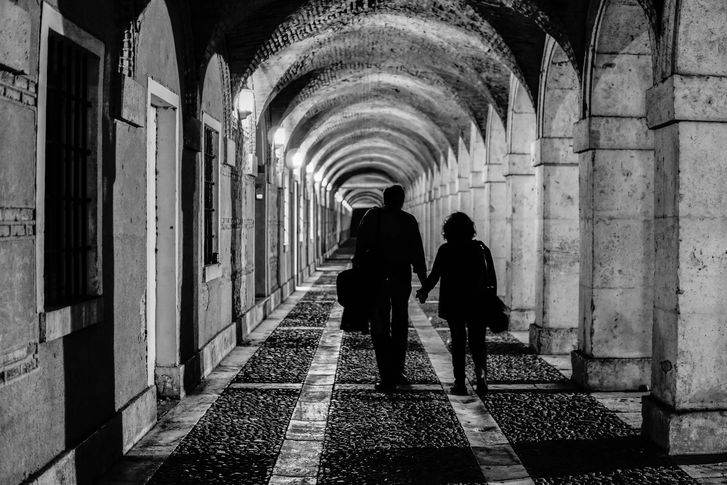 Palacio Real de Aranjuez - Under the arches, two silhouettes walk hand in hand — where light and shadow carve the path of intimacy.
