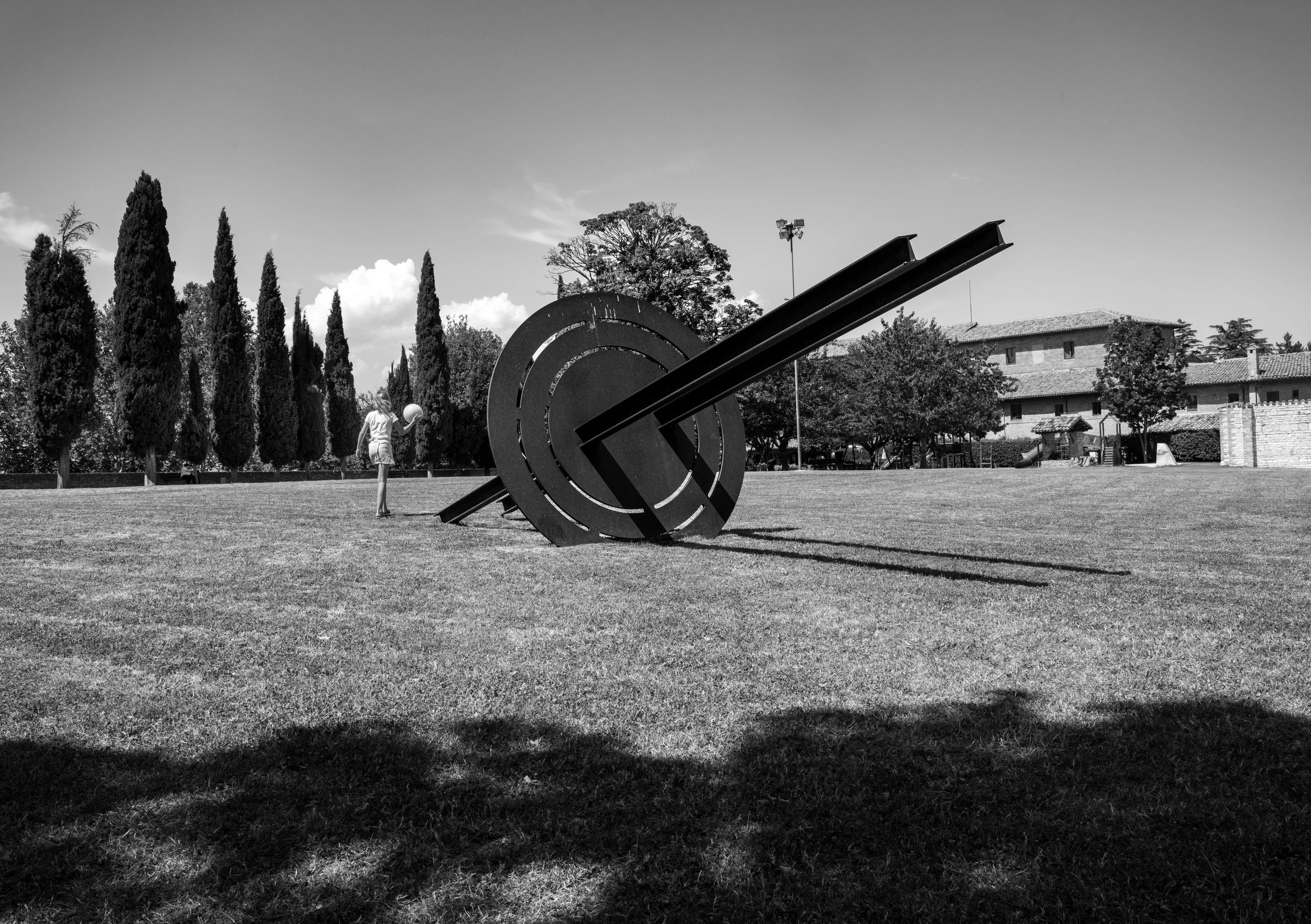Urbino - Amid steel and stone, a child plays; innocence softens edges where time carves silent monuments.