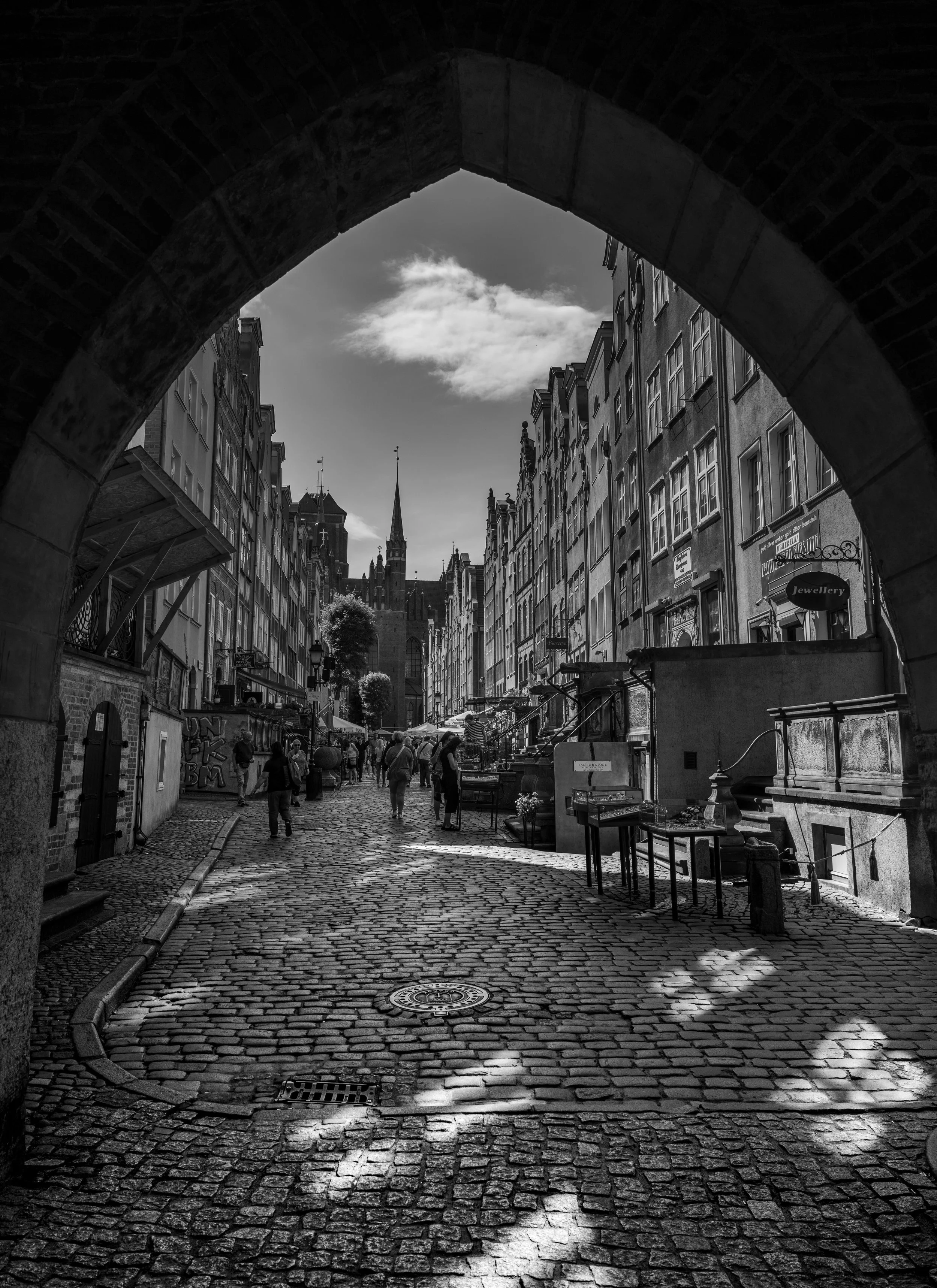 Gdańsk - Through ancient arches, cobblestones glow; shadows guide footsteps toward spires, where history breathes within the light.