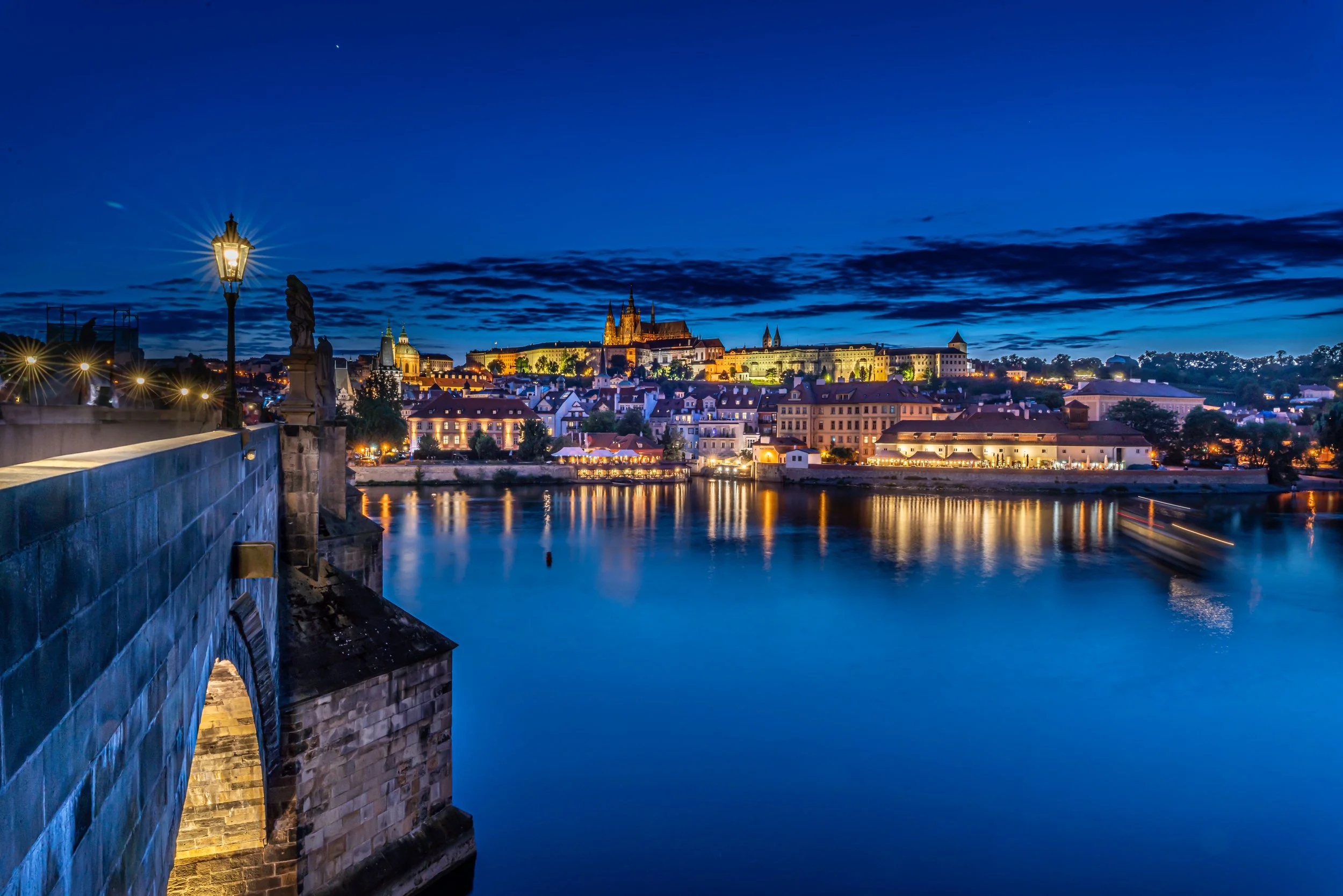 Prague, Vltava River - Lights shimmer across water, echoing empires and saints, where history drifts with silent waves.