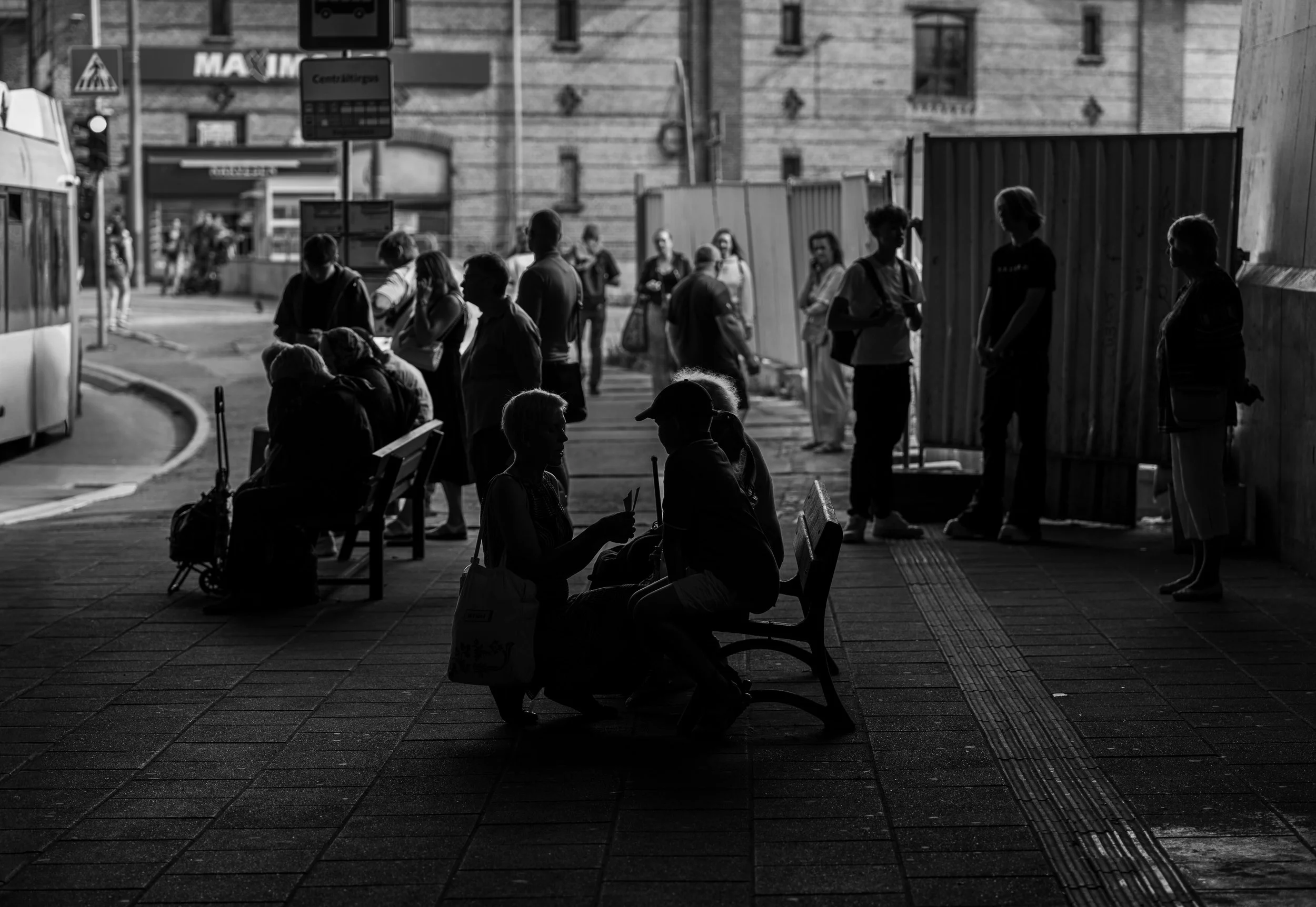 Riga - Beneath concrete shadows, lives intertwine; waiting becomes a quiet stage where fleeting stories softly emerge.