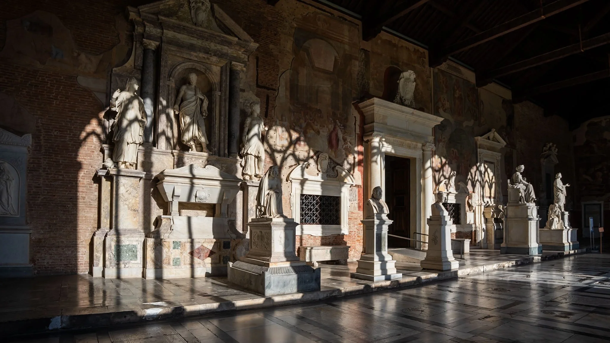 Pisa, Camposanto: Marble tombs and statues etched in shadow.
