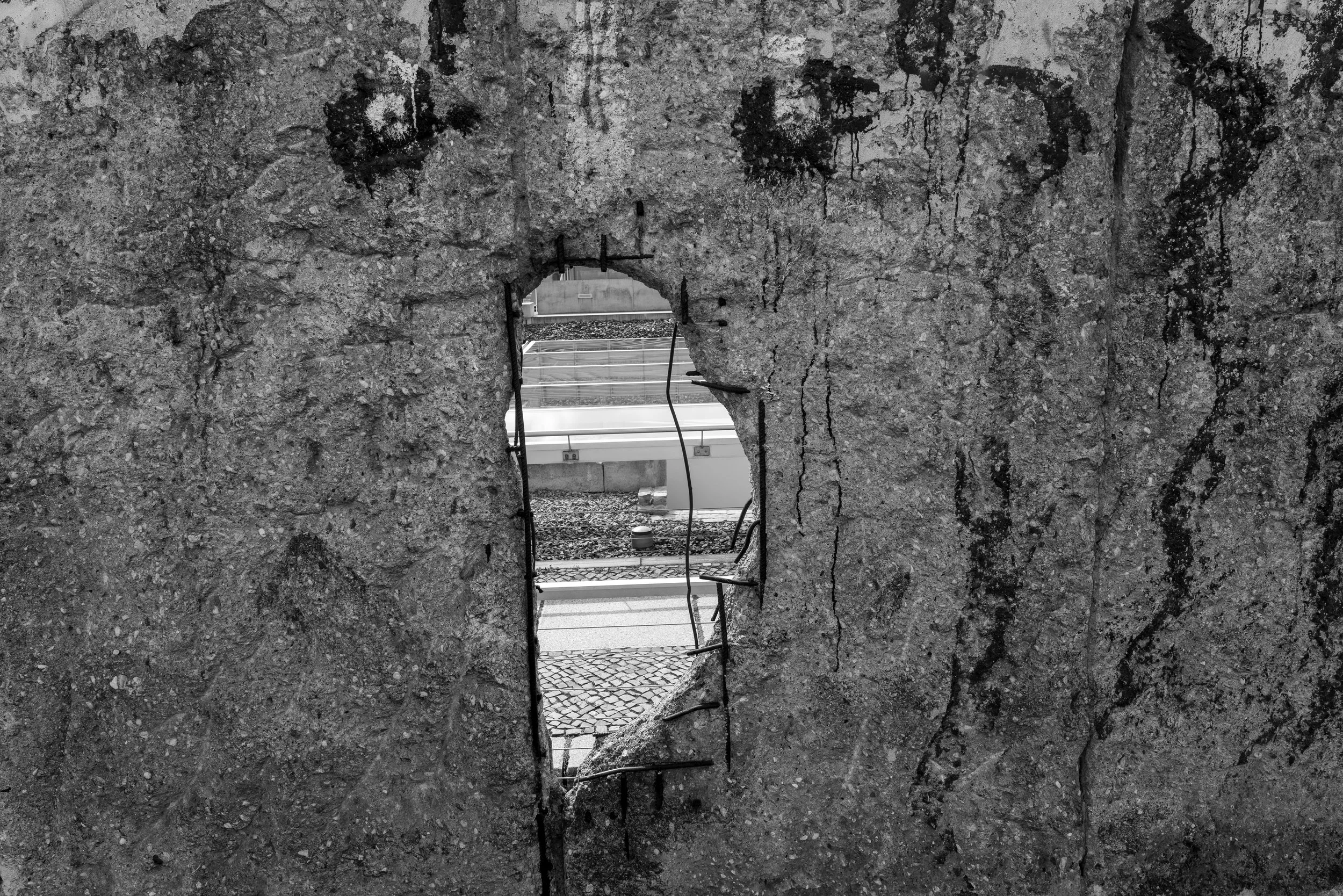Berlin – Shattered wall, exposed steel veins, memory of division pierced by glimpses of another world.