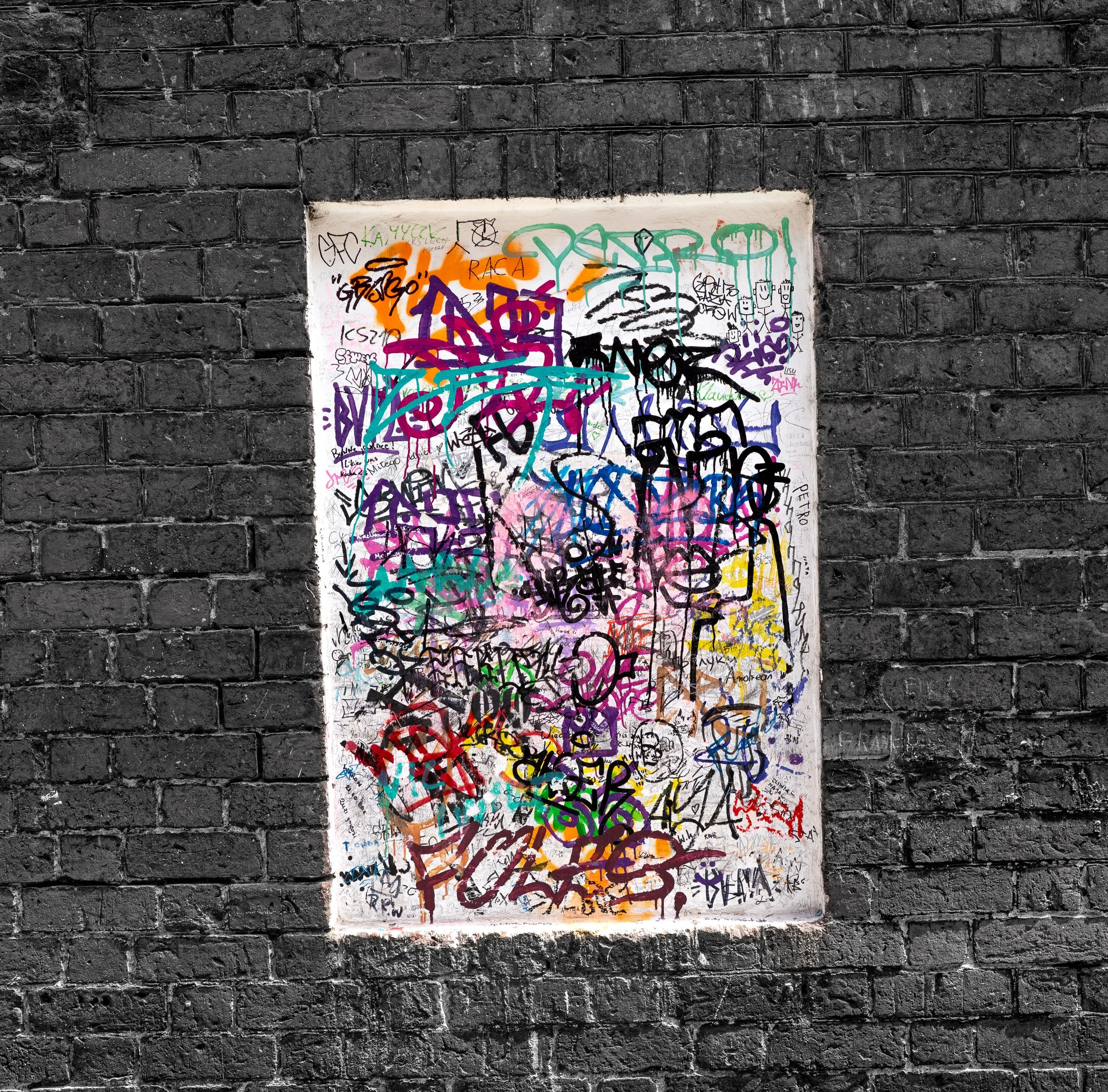 Prague – Graffiti blooms on dark brick, fragments of defiance painting memory with raw, untamed light.
