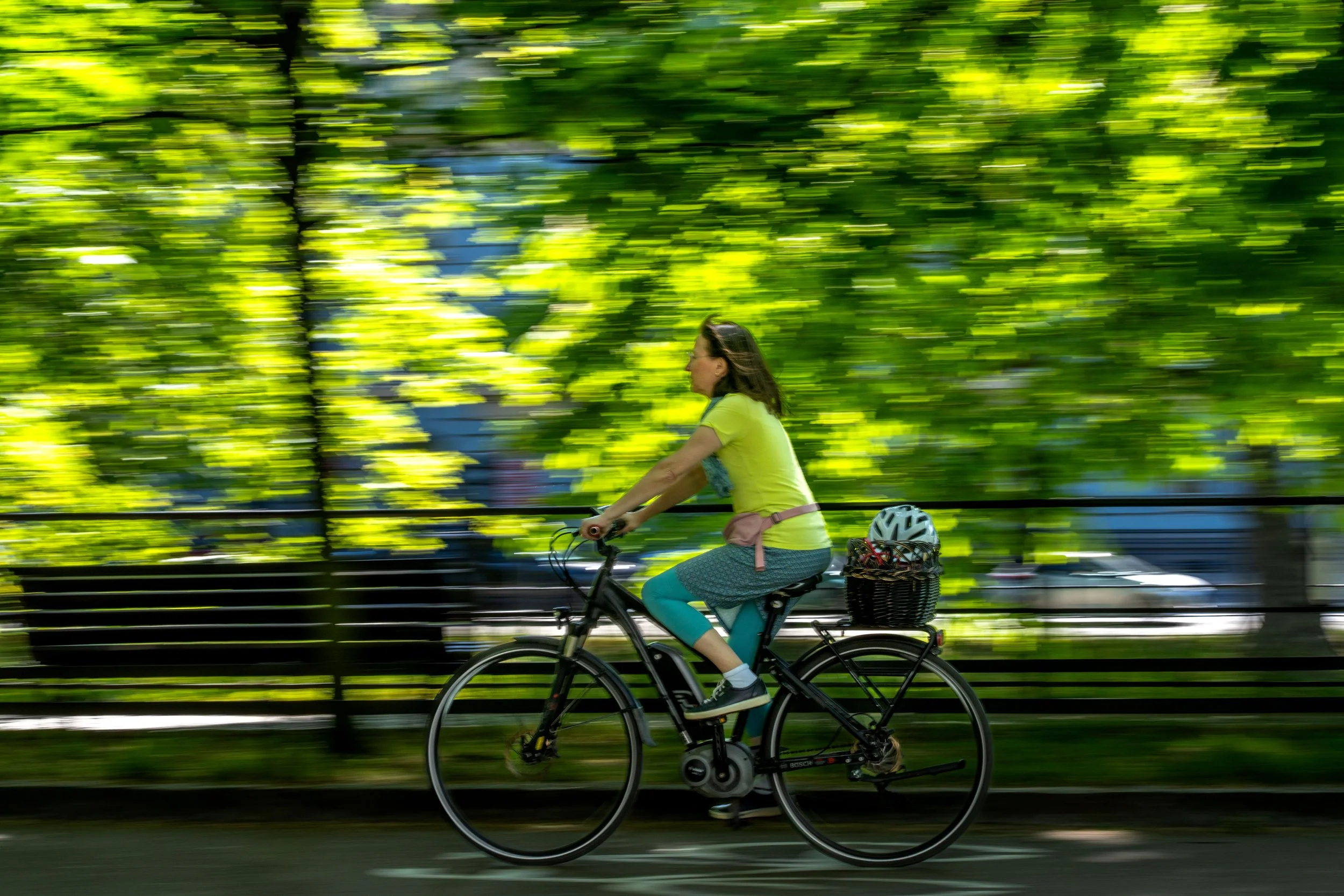 Wroclaw - Wheels spin through green shadows, a fleeting figure woven into summer’s living tapestry.