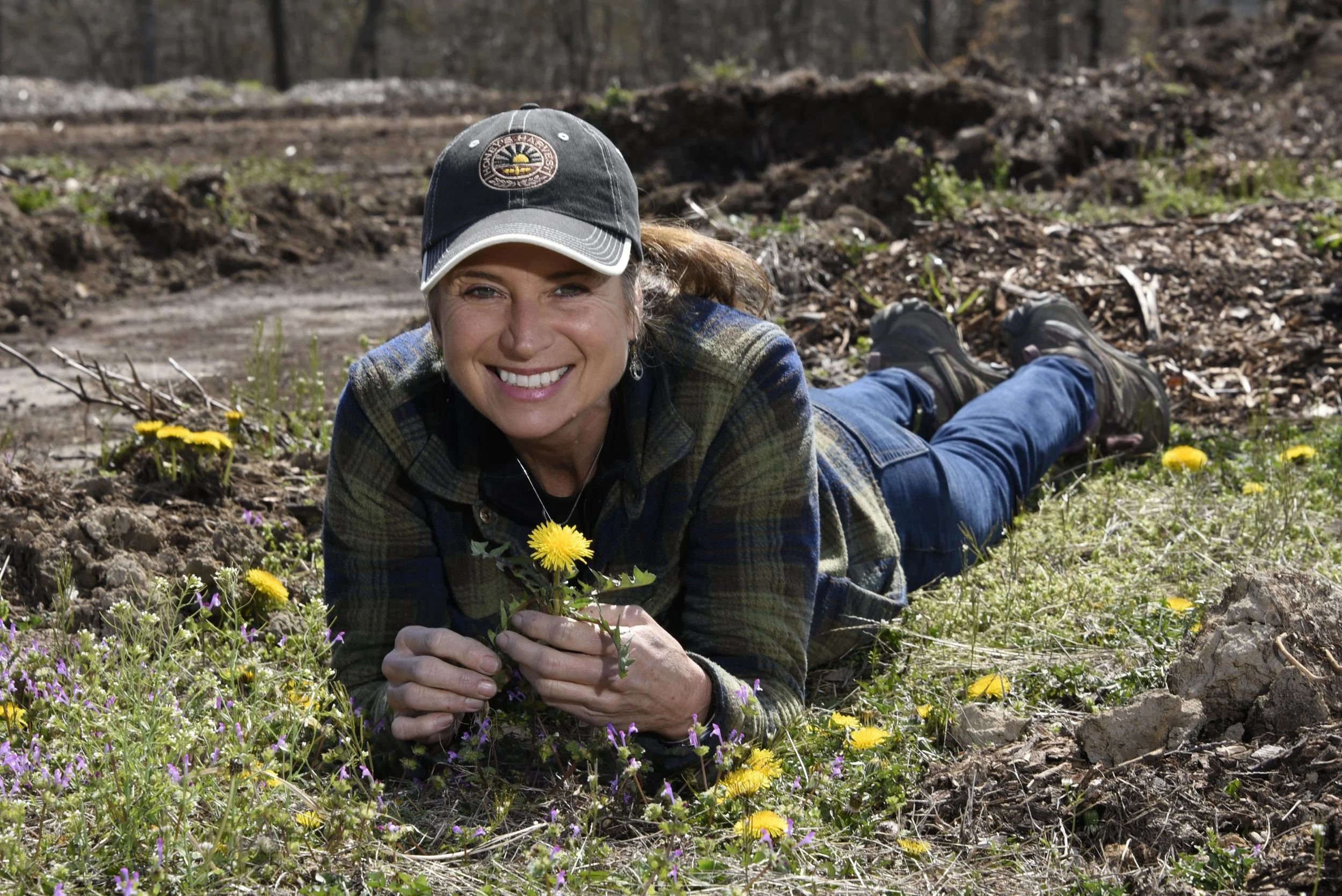 Smiling woman laying on the ground holding a dandelion