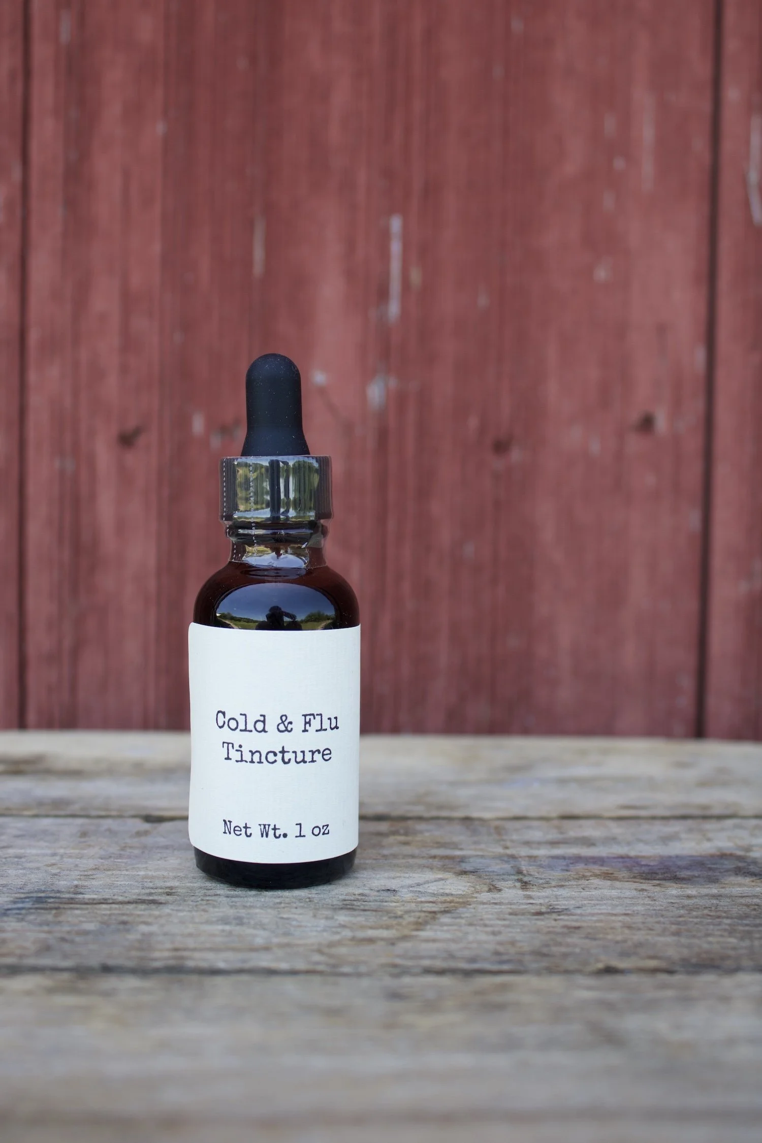 Bottle of Cold & Flu Tincture on a wooden surface in front of a red wooden background