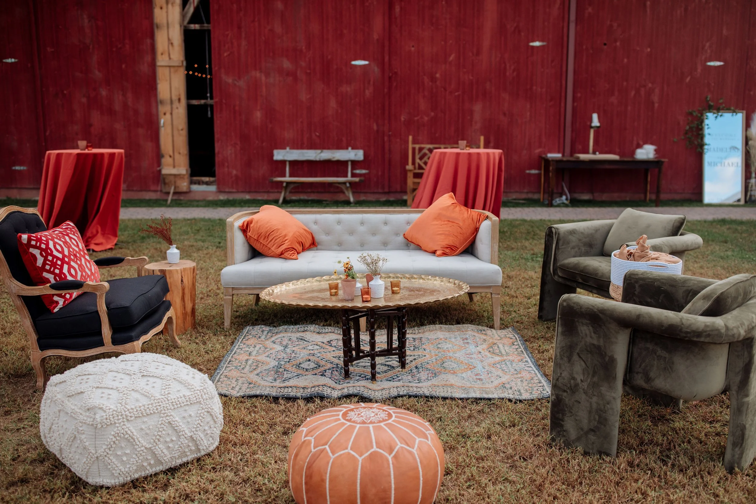 Couch and armchairs arranged outdoors in front of a red barn wall
