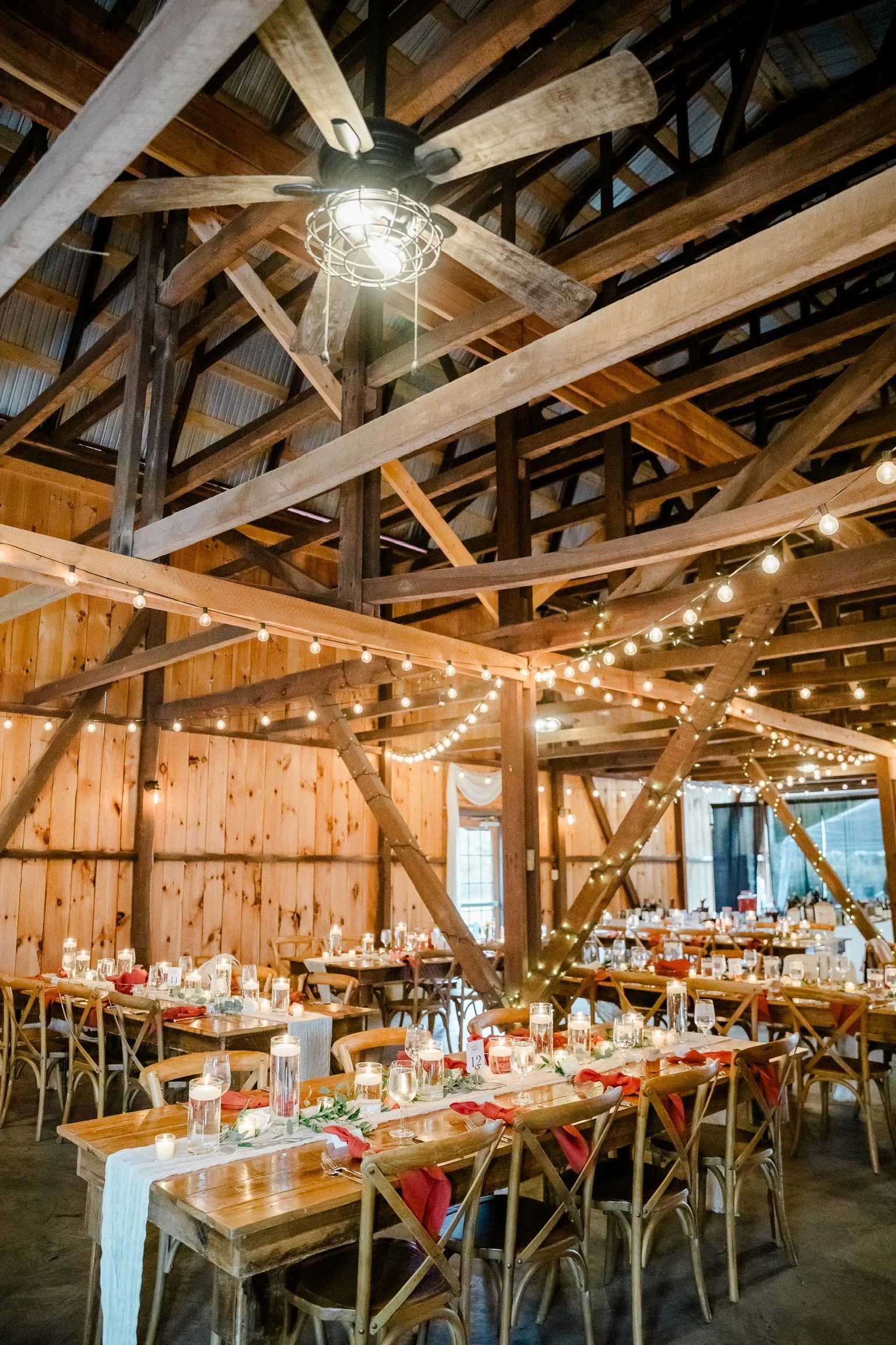 Interior of a barn set up with tables for dinner with bistro lights strung in the rafters