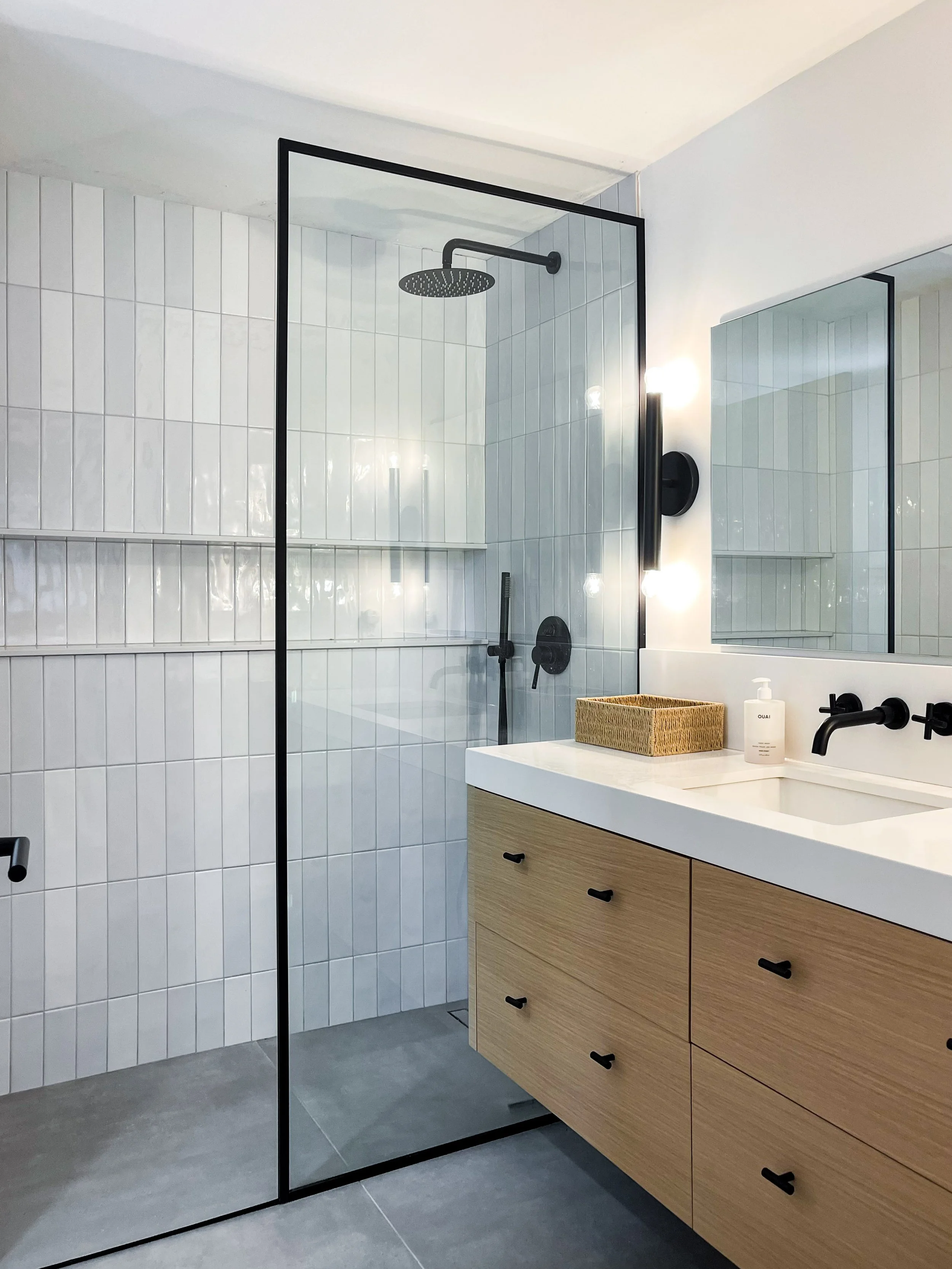 Frameless glass shower enclosure in modern Vaughan bathroom remodel featuring white subway tiles, black fixtures, and built-in niche
