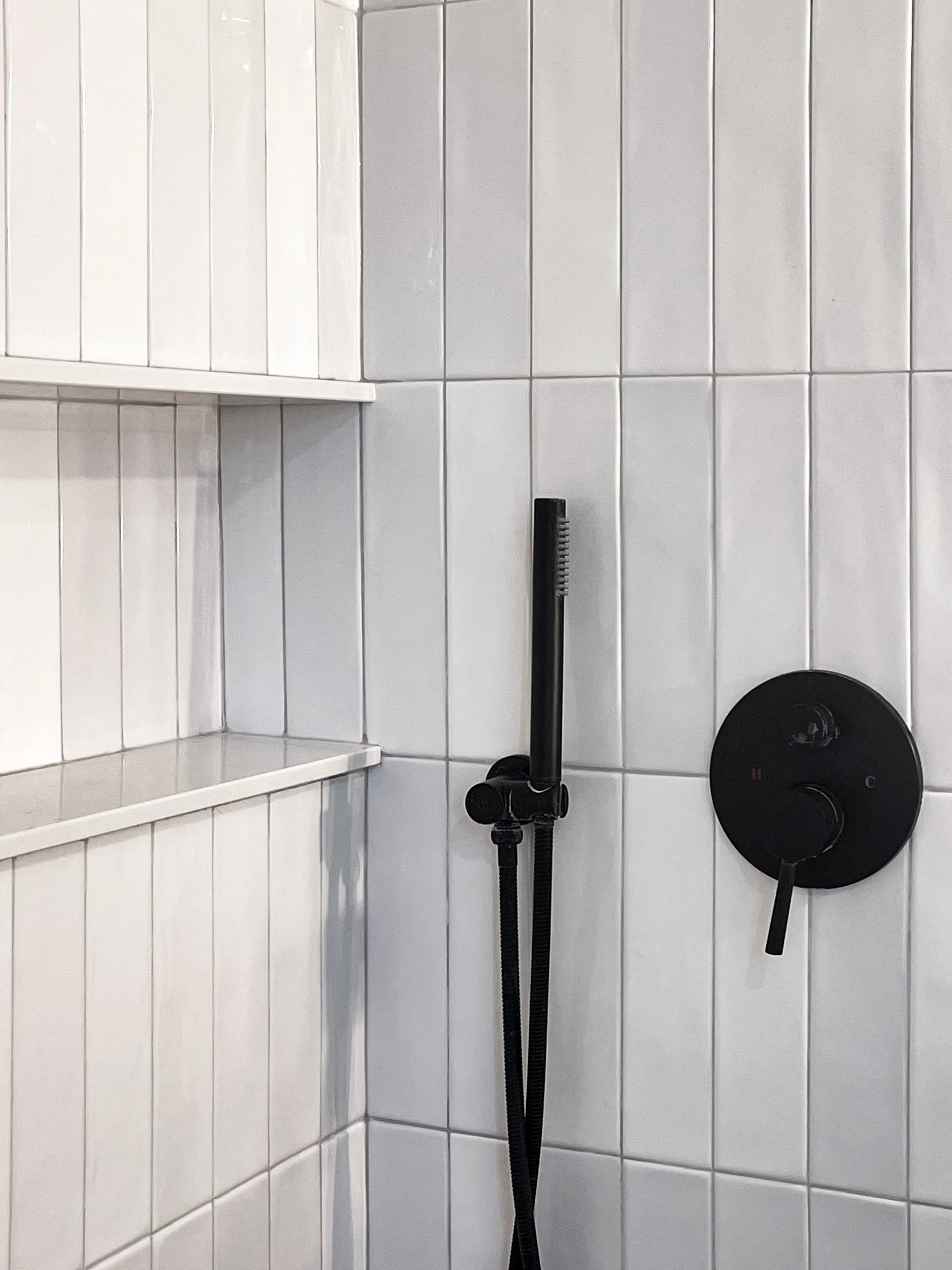 Close-up of black matte shower valve and handheld wand in renovated Vaughan bathroom with white subway tiles and recessed storage niche