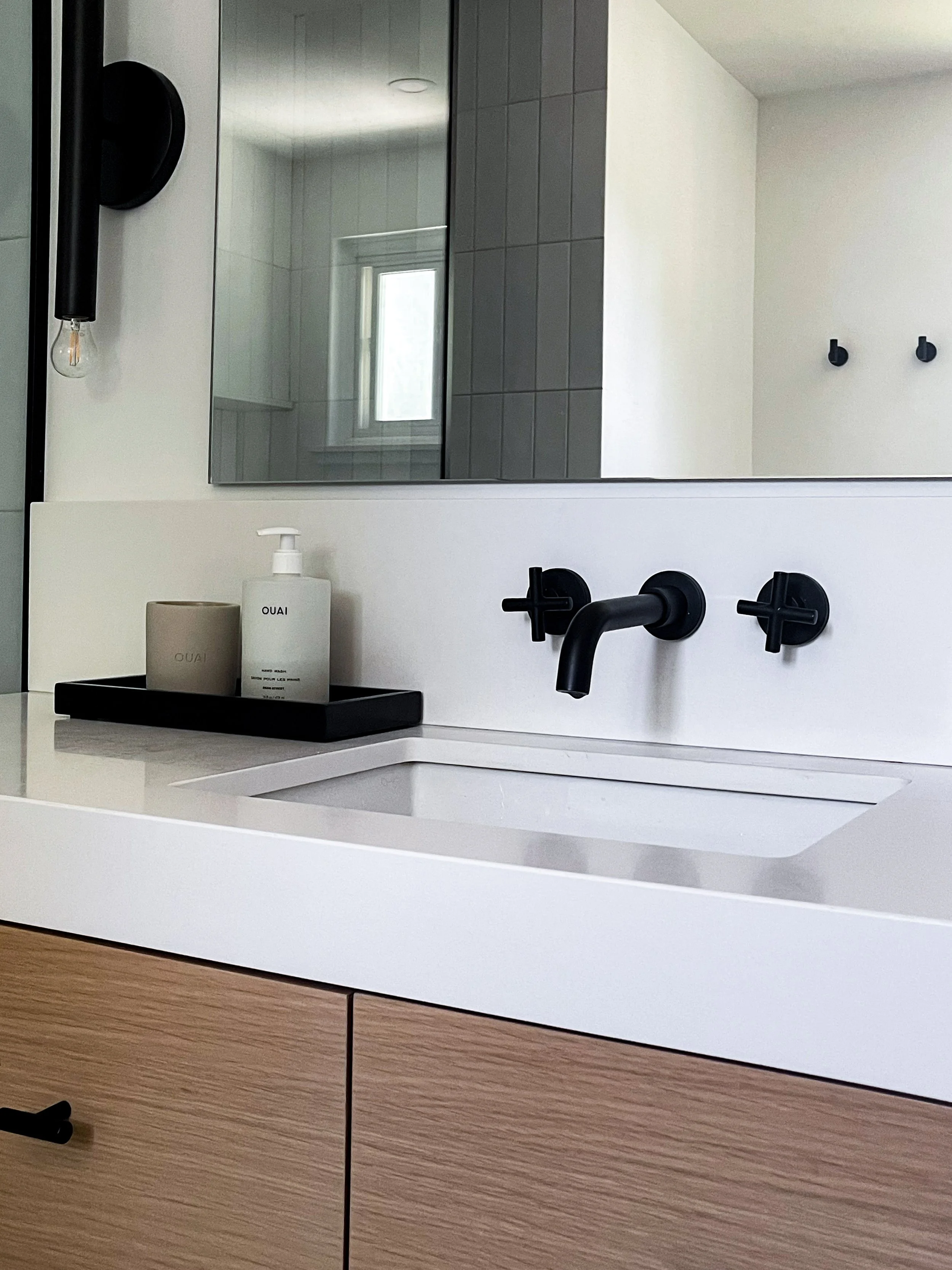 Sleek wood vanity with white quartz countertop, black matte faucet, round black-framed mirror, and globe sconces in Vaughan bathroom renovation