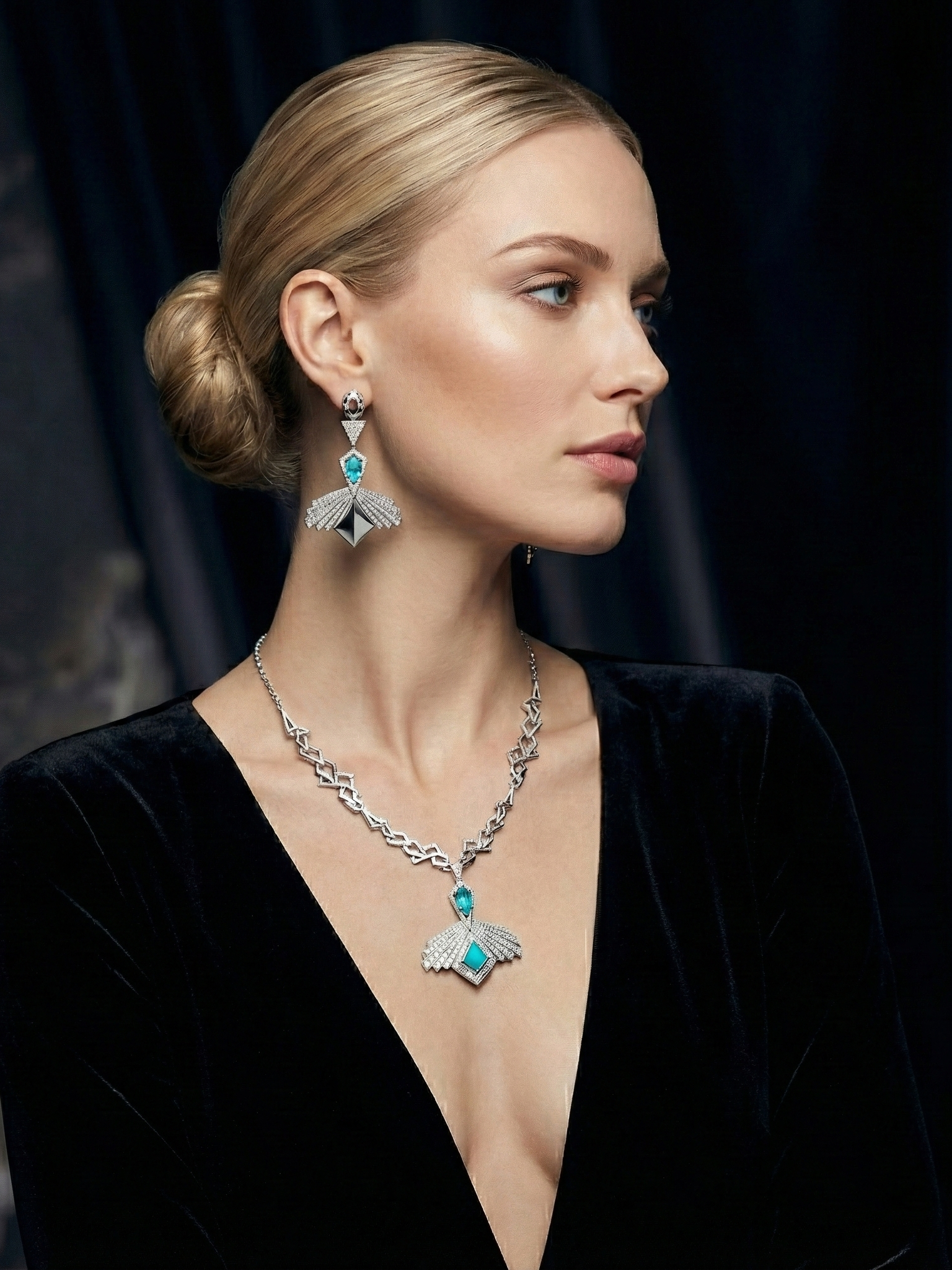 A woman with blonde hair styled in a low bun wearing a black dress and silver jewelry featuring turquoise stones. She has matching earrings and a necklace with bird and wing motifs, displaying a luxurious and elegant style.