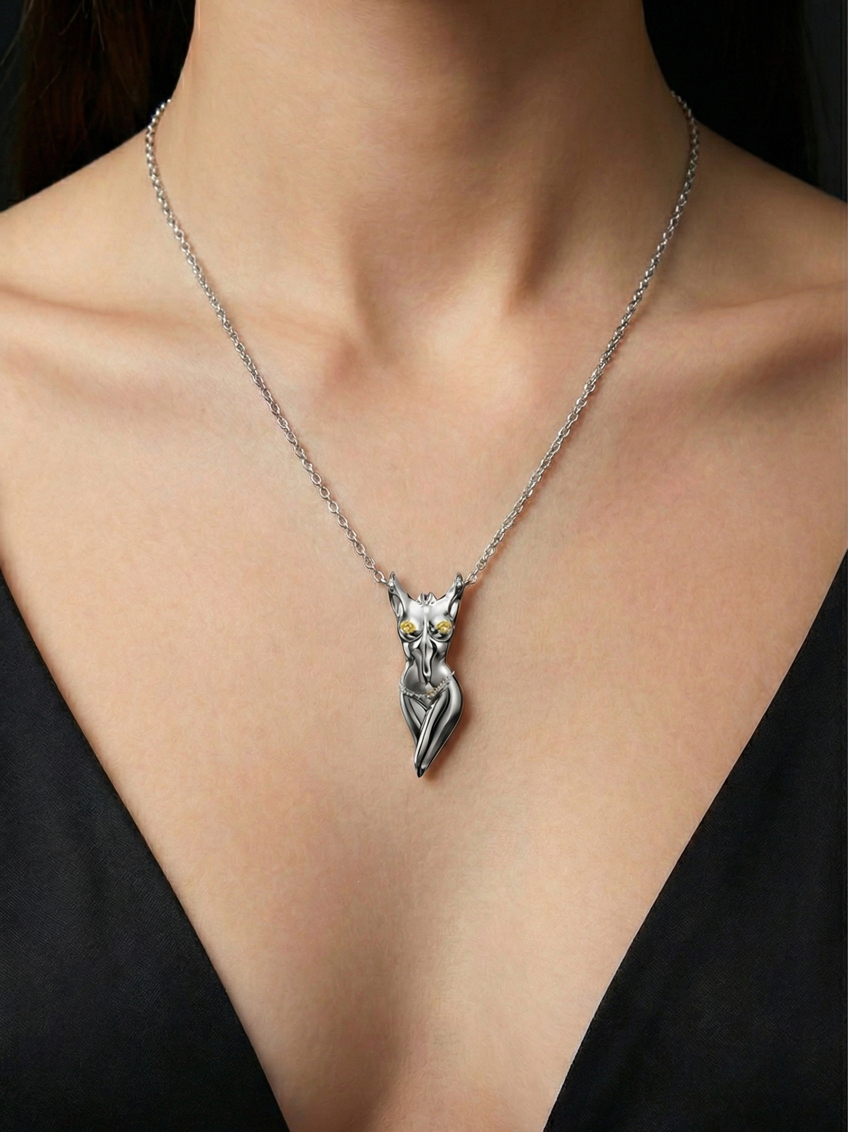 A close-up of a woman wearing a silver necklace with a cat-shaped pendant, featuring gold-colored eyes, set against a black top.