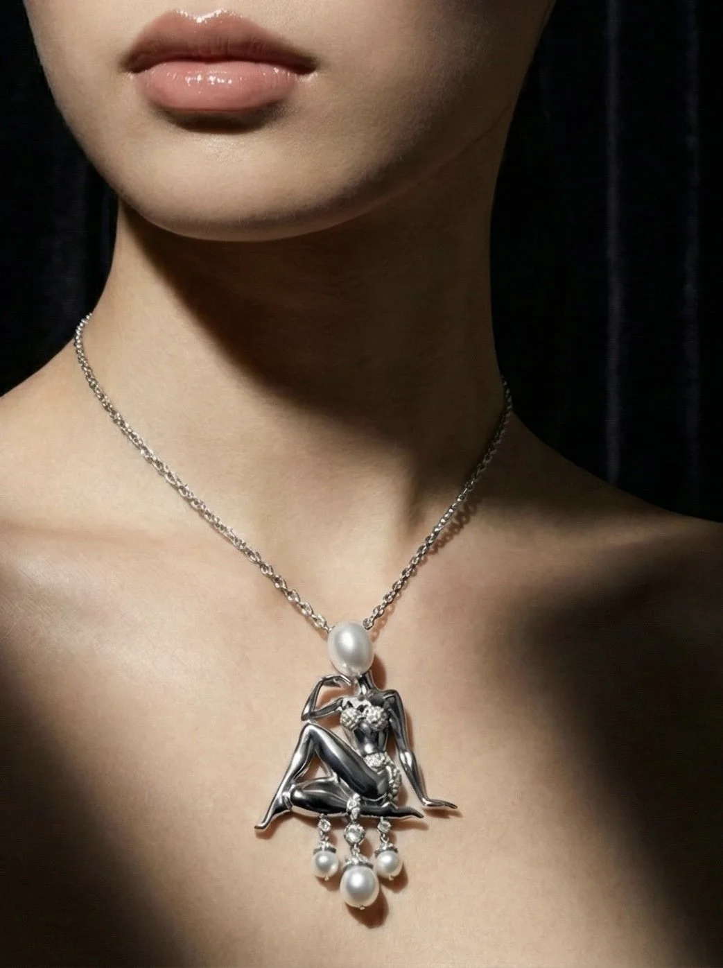 Close-up of a woman's neck and collarbone wearing a silver necklace with a pendant of a woman sitting, embellished with pearls and small diamonds.