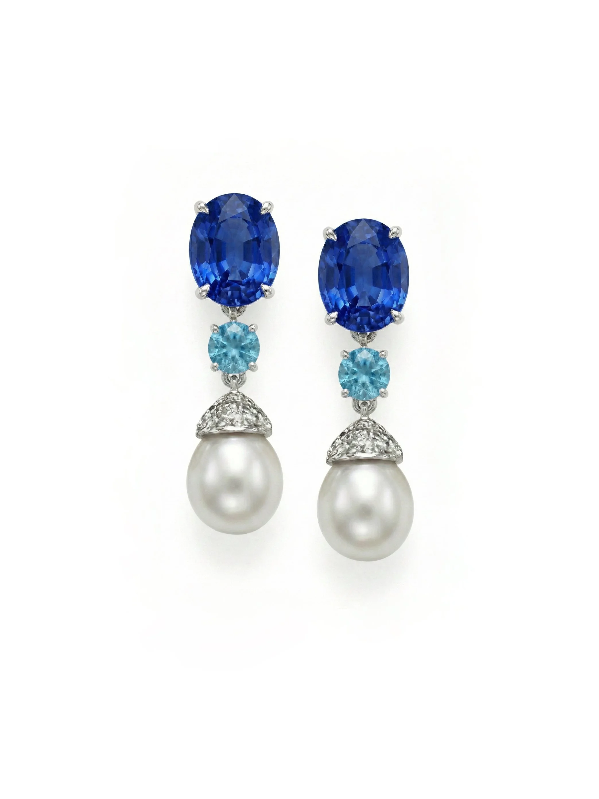Pair of drop earrings featuring large oval blue sapphires, smaller round blue topaz, and white pearls with diamond accents on a white background.