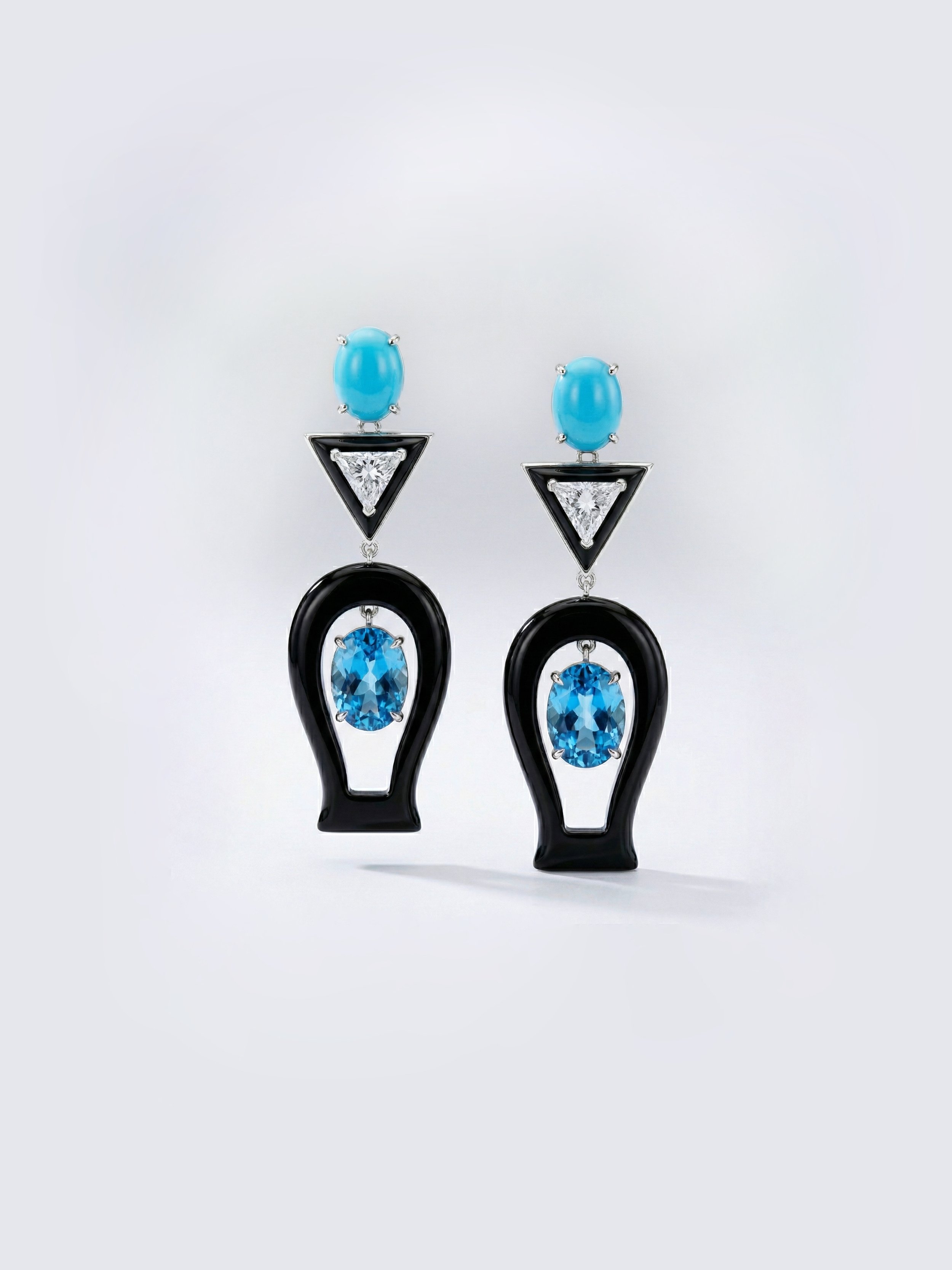 Pair of statement earrings featuring black, blue, and clear gemstones in geometric shapes on a plain white background.