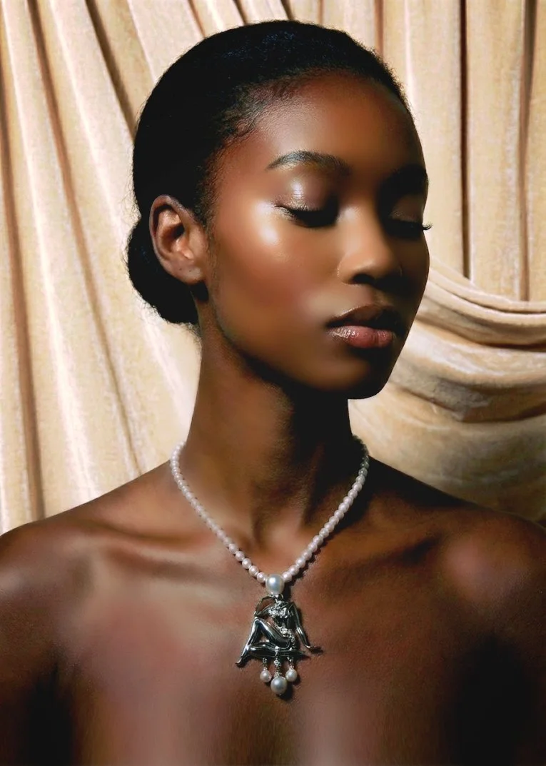 A woman with dark skin and smooth hair styled back, wearing subtle makeup, a pearl necklace with a large pendant, and no visible clothing from the shoulders up, standing against a golden curtain background.