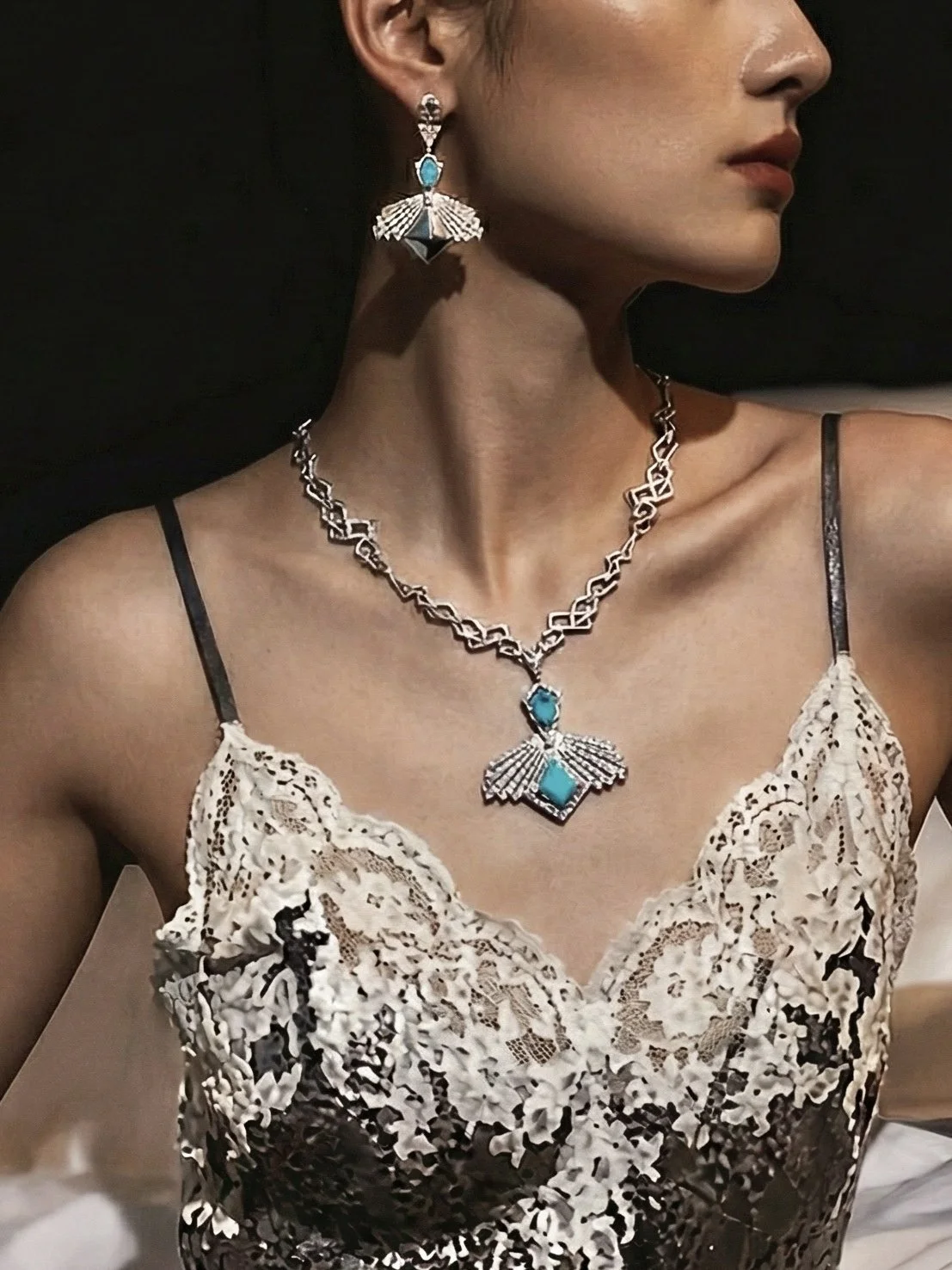 A woman wearing turquoise and silver jewelry, including earrings and a necklace, and a cream-colored lace top with dark spaghetti straps.