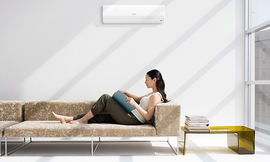 Women lounged on couch reading. Hitachi high wall heat pump unit in background.
