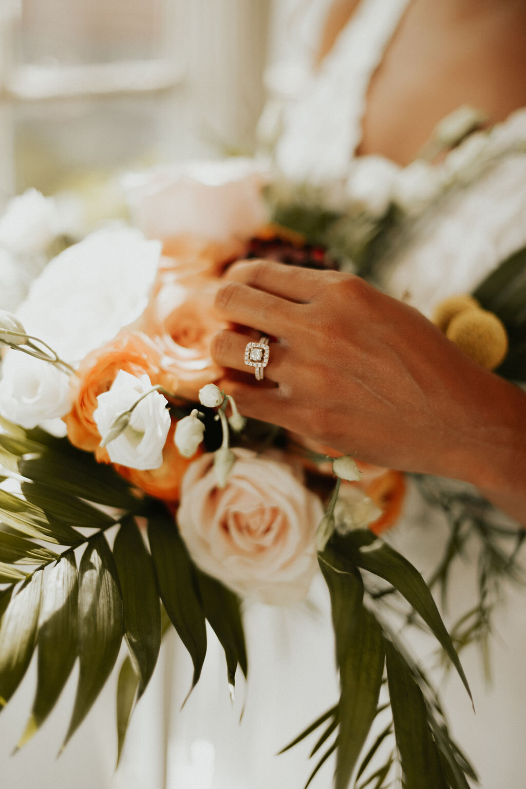 A bride's left hand near her bouquet taken by Courtney Mitchell Photo showcasing her diamond engagement ring and wedding band.