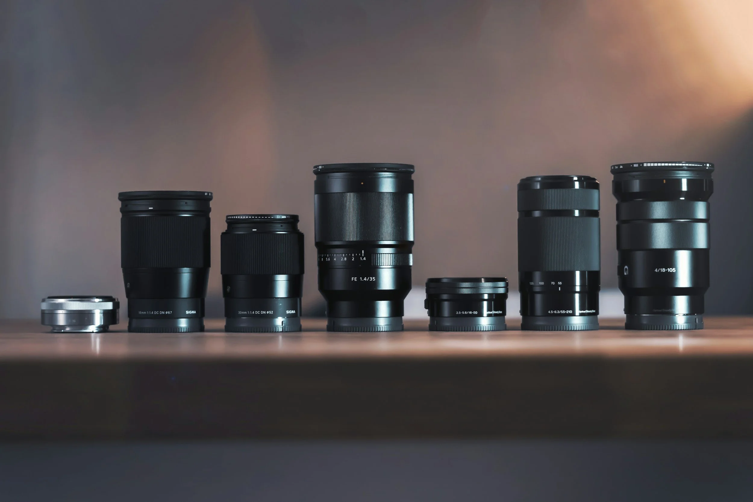 A row of camera lenses on a wooden surface in soft directional light