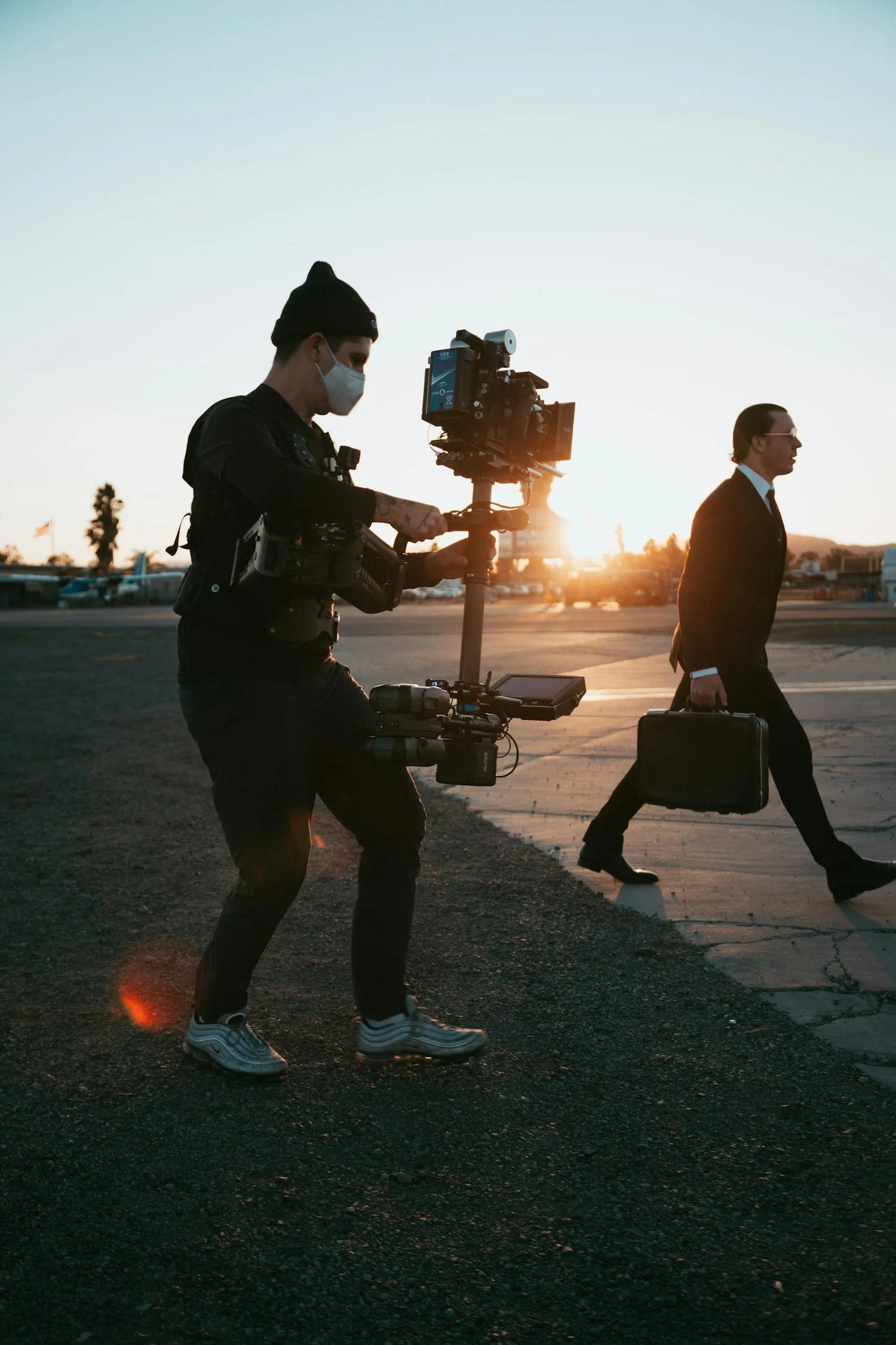 Camera operator filming a businessperson on a city walkway at sunset