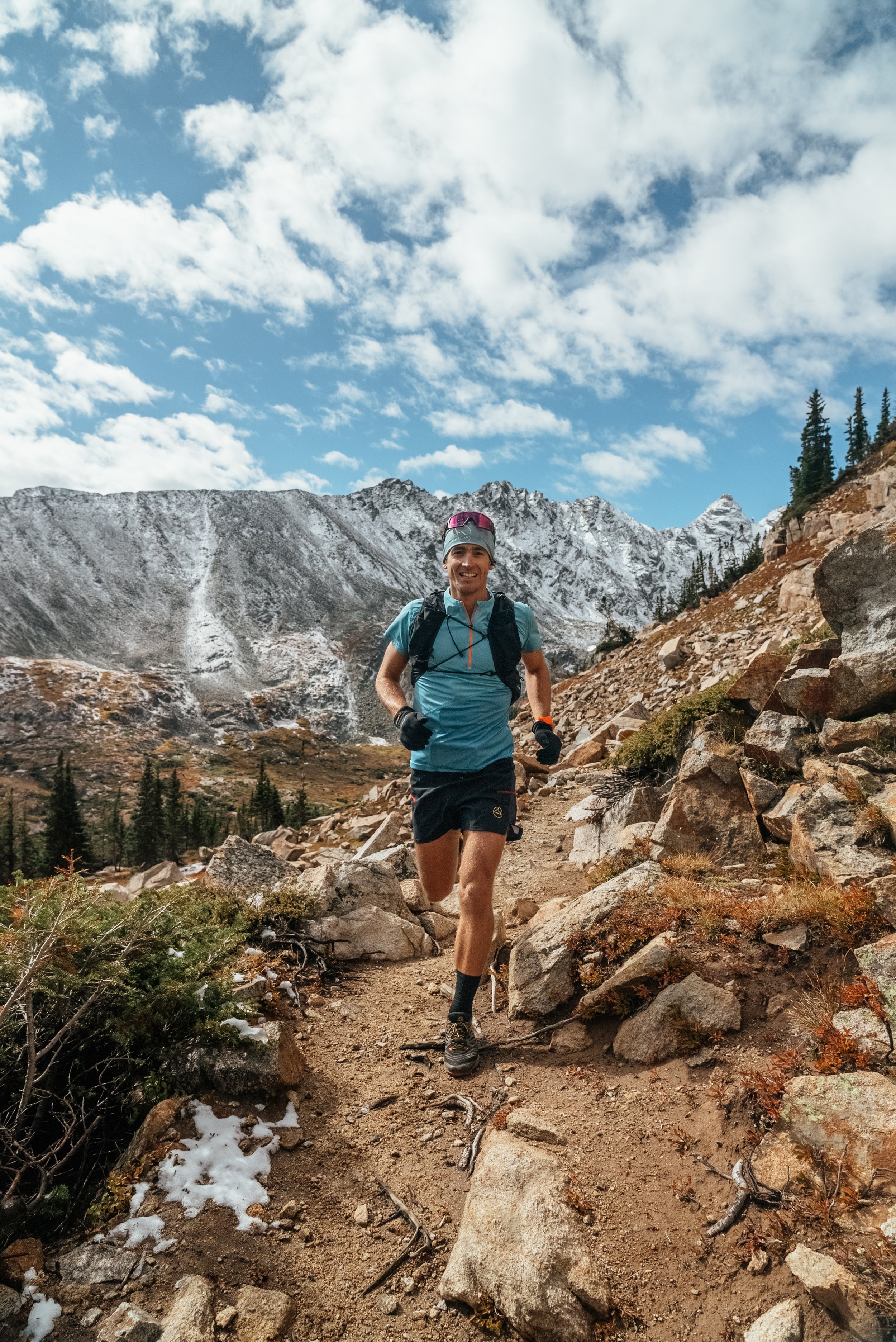 Runner following a rocky mountain trail beneath blue sky and clouds