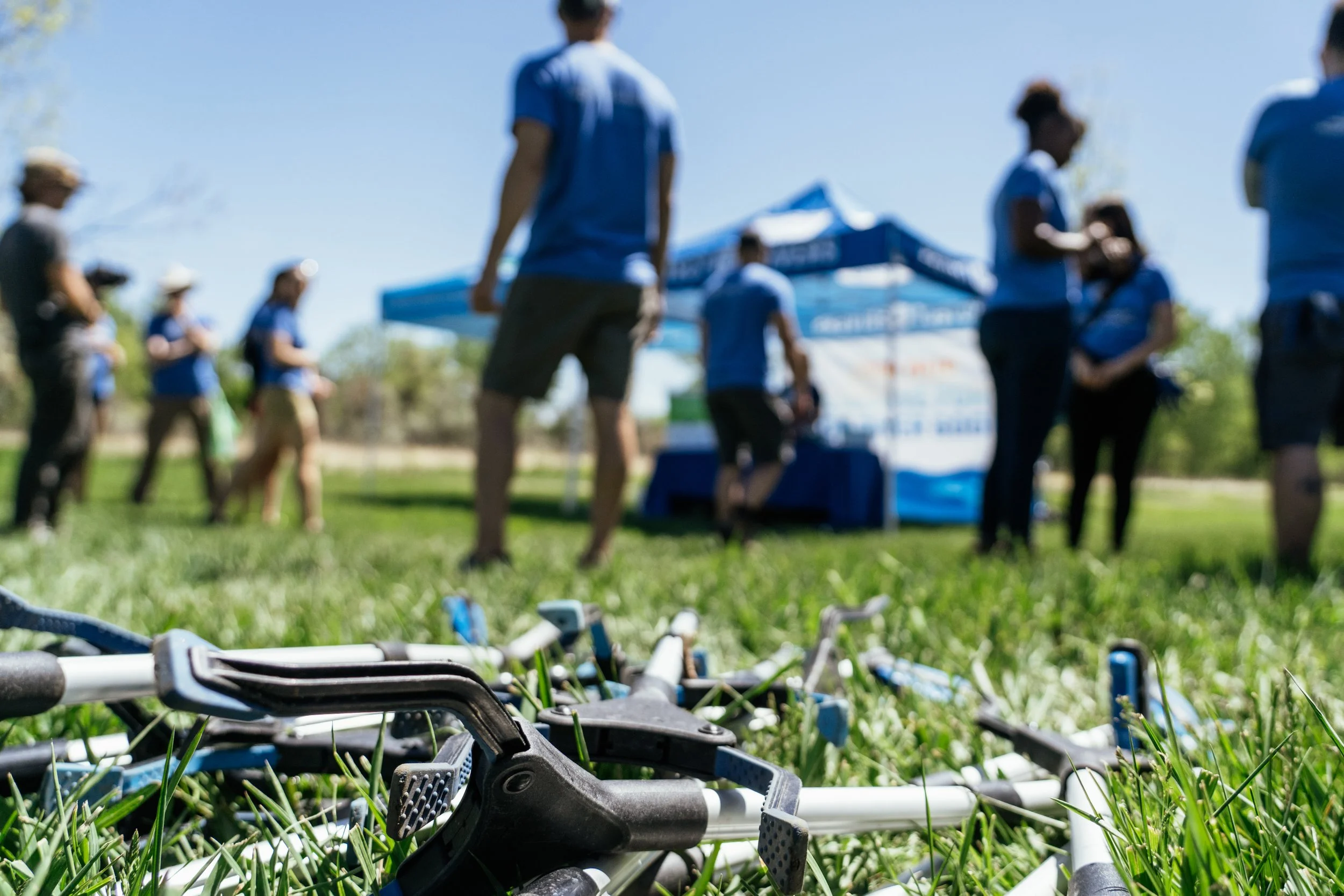 Cleanup tools in the foreground as Elevations Credit Union volunteers gather beneath a blue event tent