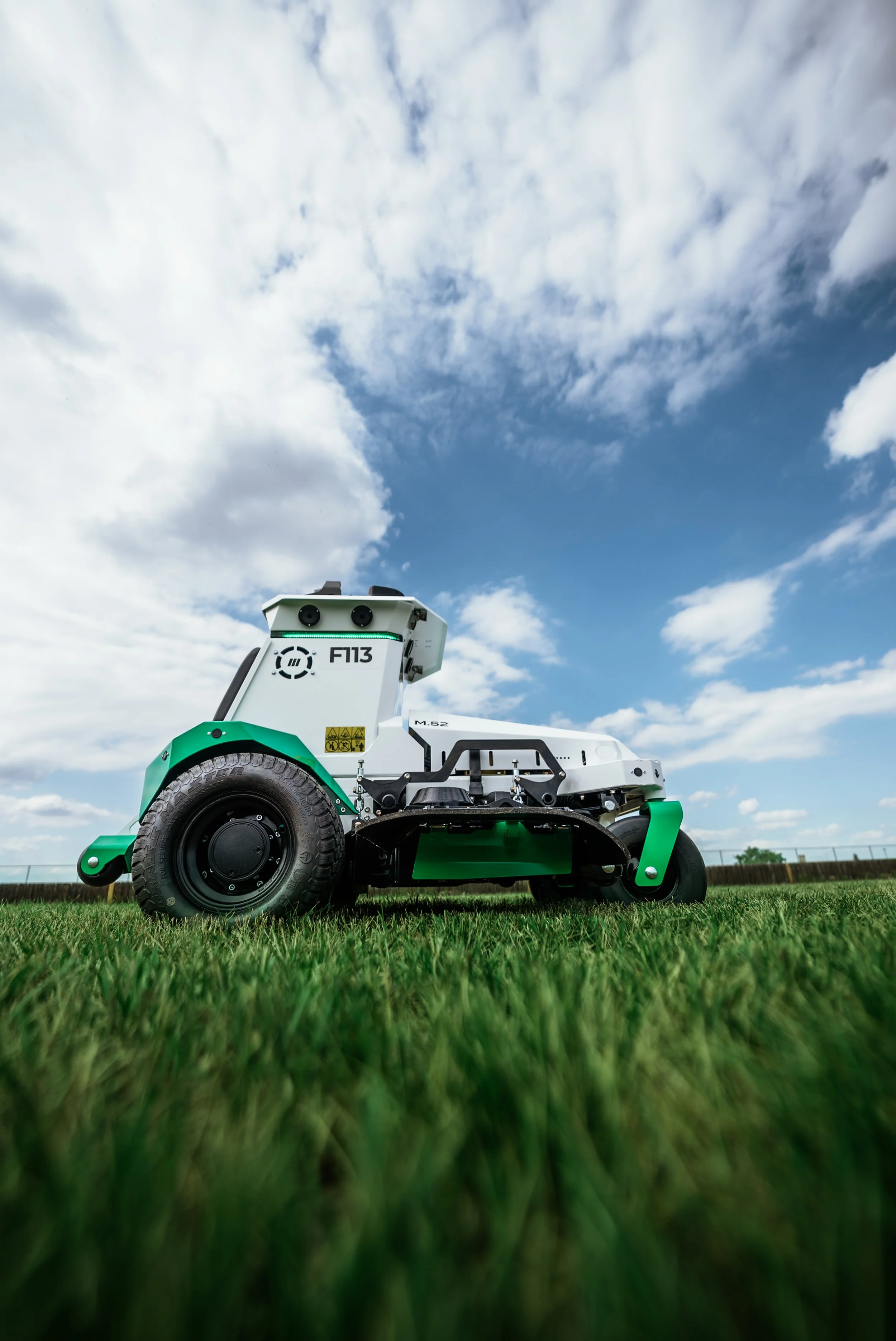 A robotic lawn mower on a grassy field under a partly cloudy sky.