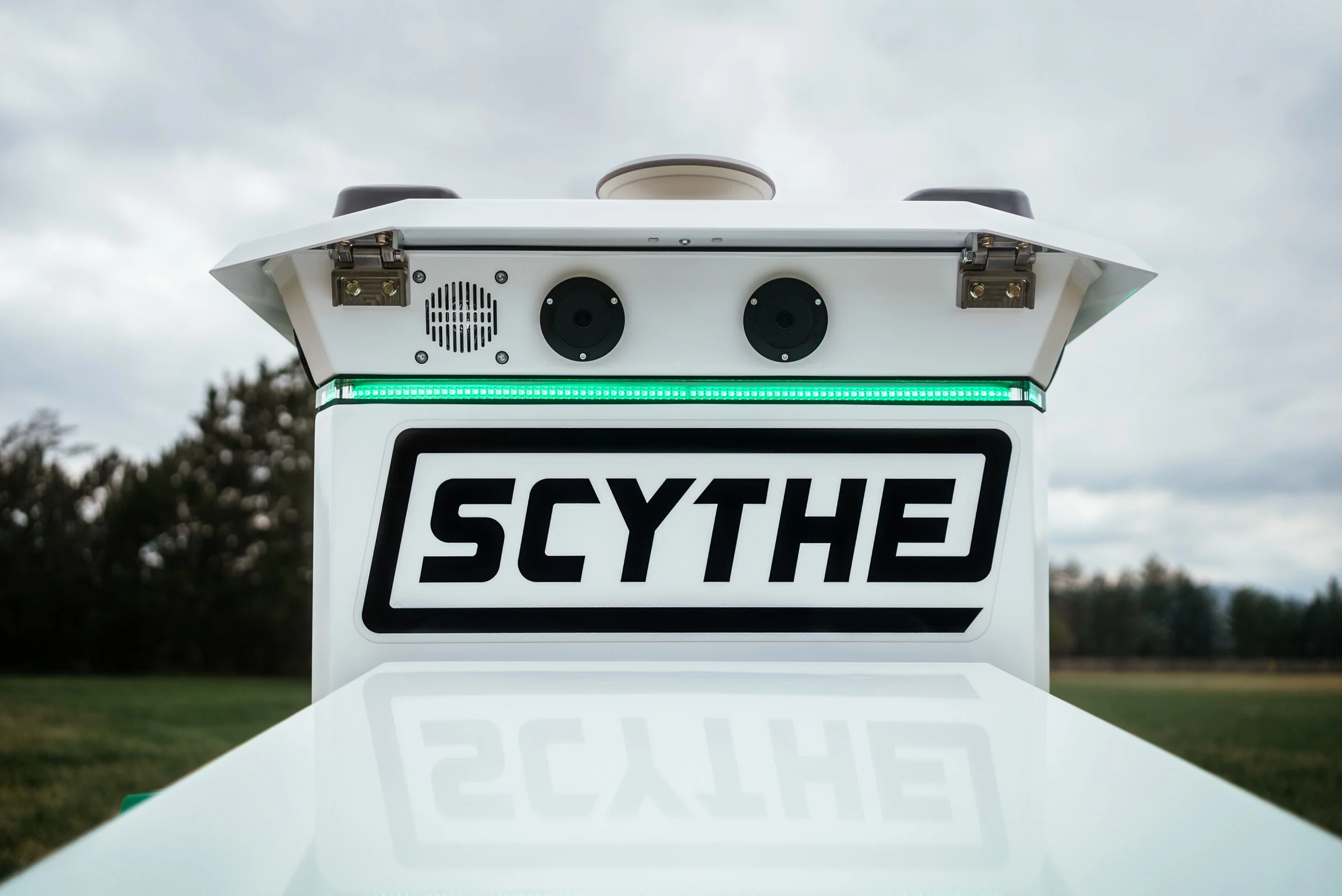 Close-up of a Scythe robotic mower showing its front sensors, green light, and logo