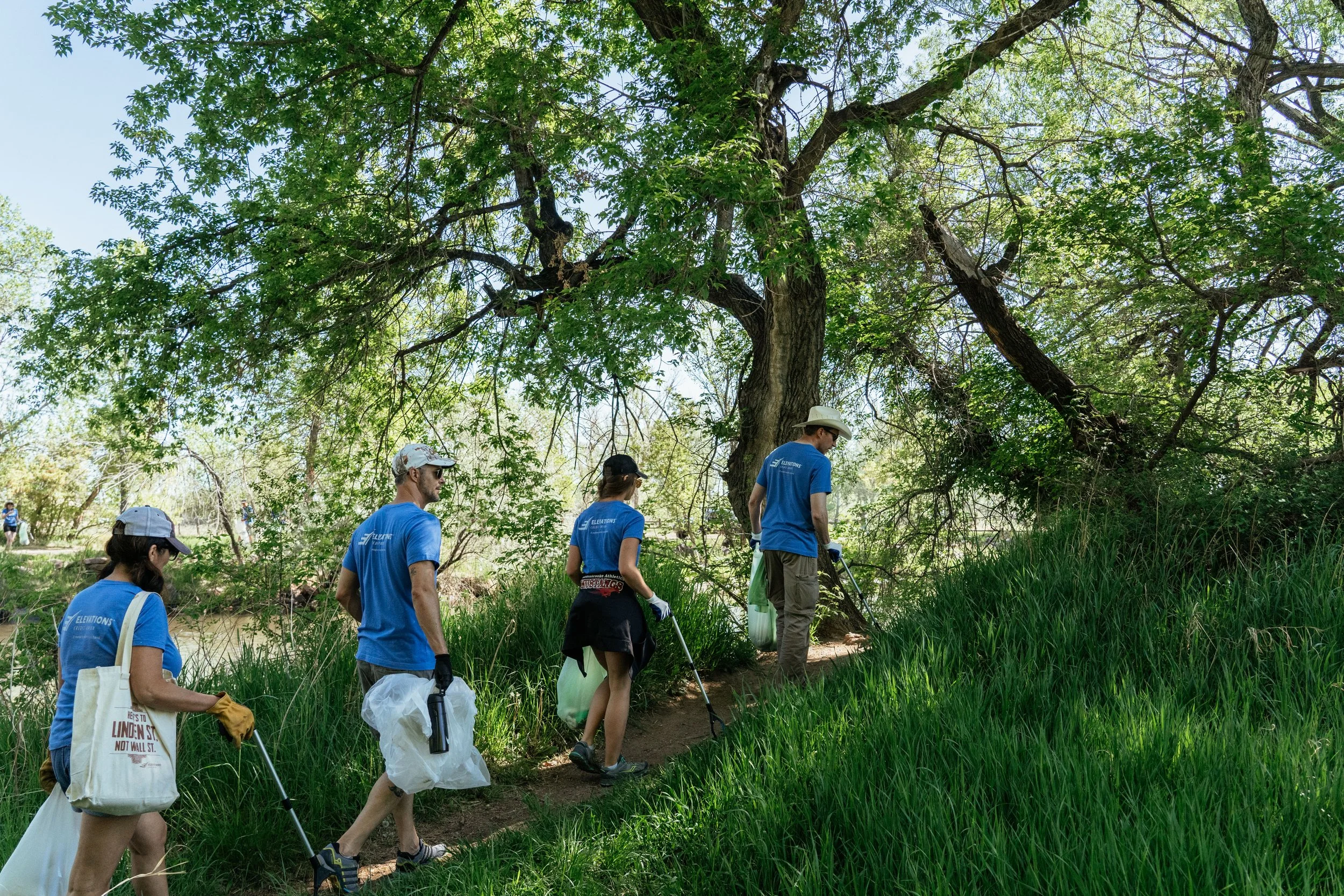 Four Elevations Credit Union volunteers carrying cleanup bags along a wooded river path