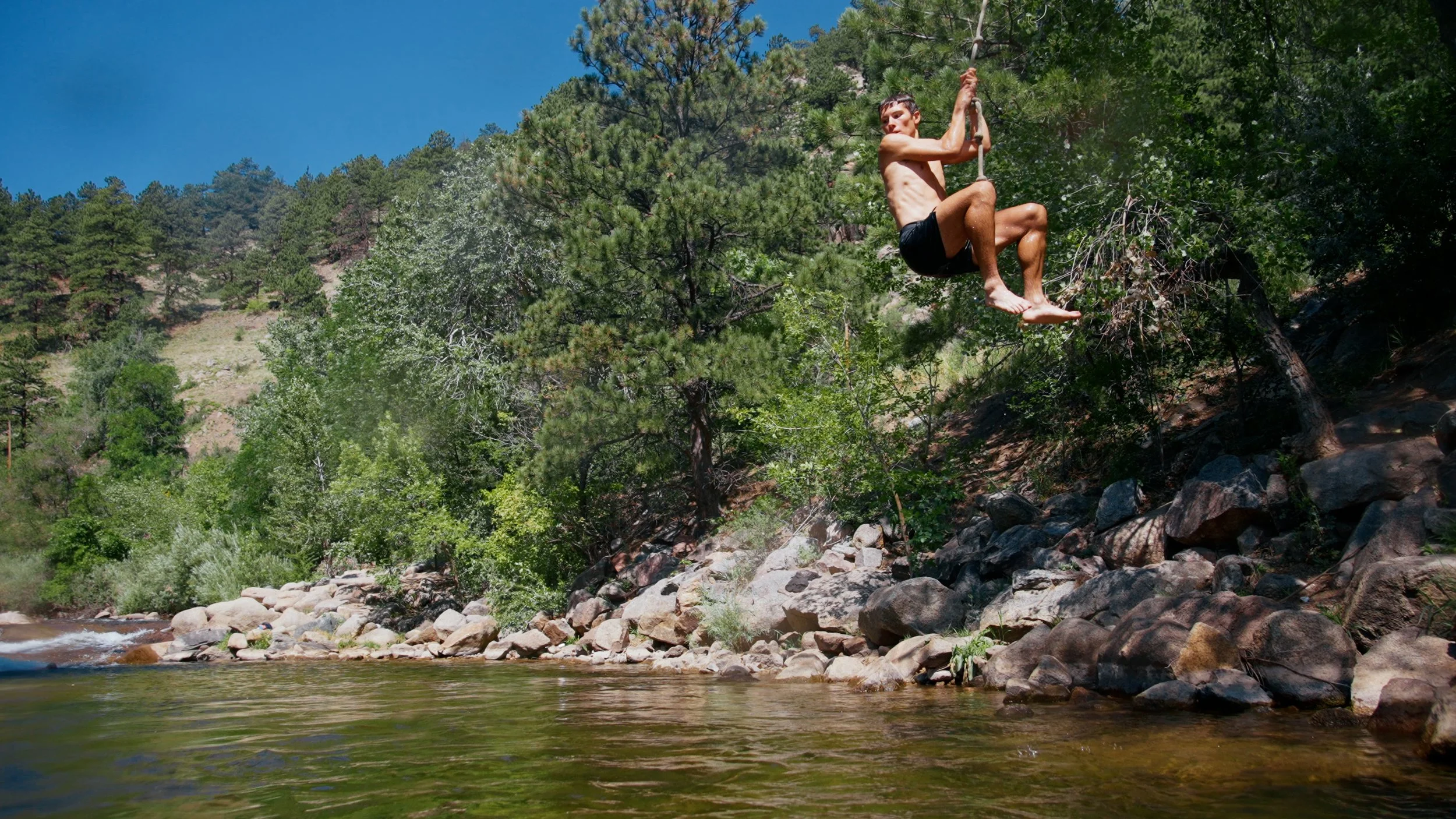 trail runner Dylan of the Trail House swinging on a rope swing above boulder creek