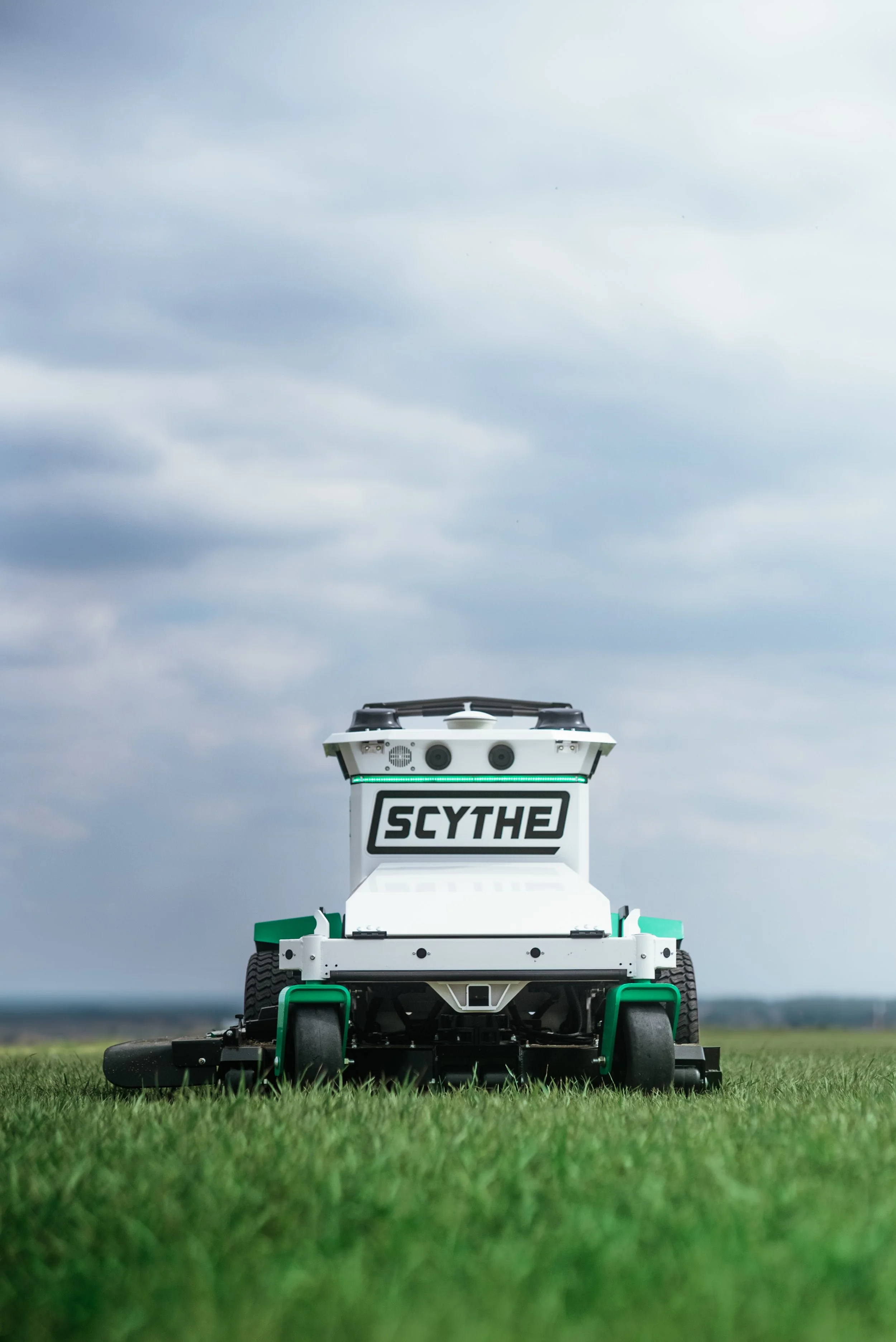Autonomous robot with the name 'Scythe' moving across a grassy field under a cloudy sky.