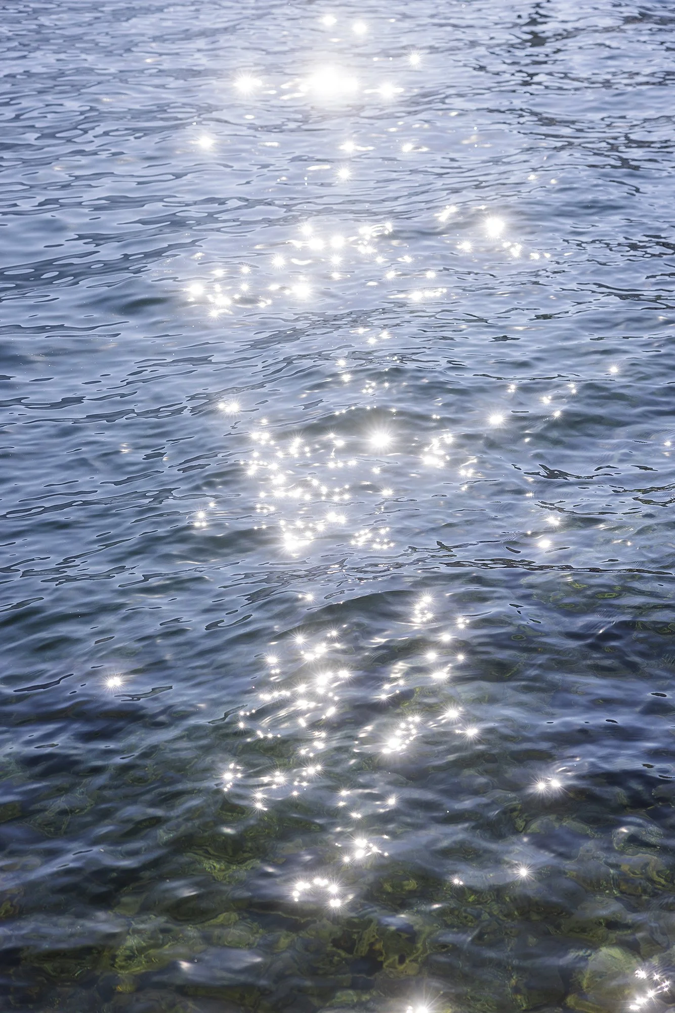 Sunlight reflecting on the surface of a clear, blue body of water with gentle ripples.