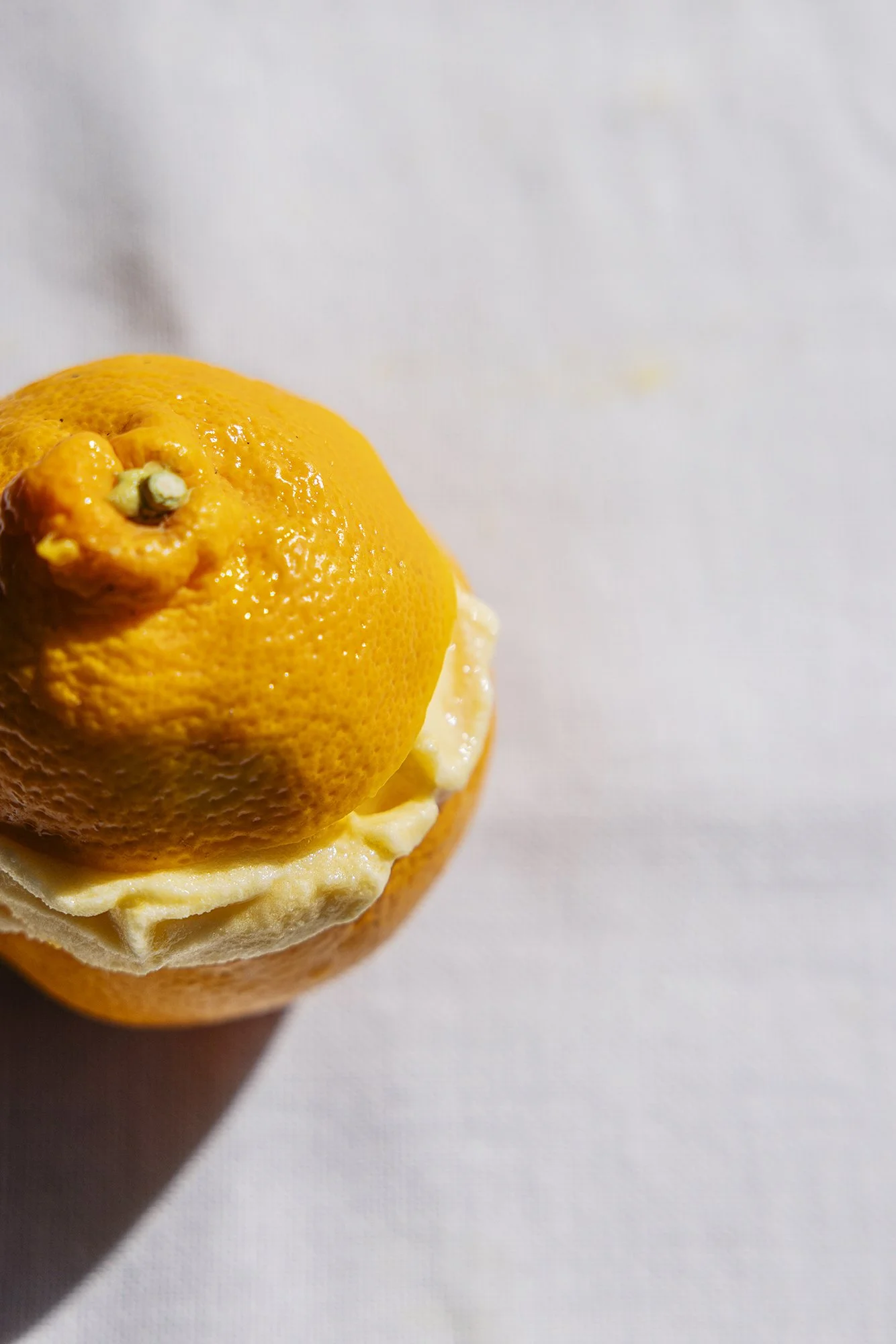 A close-up of a lemon with a bandage on the top, placed on a white surface.