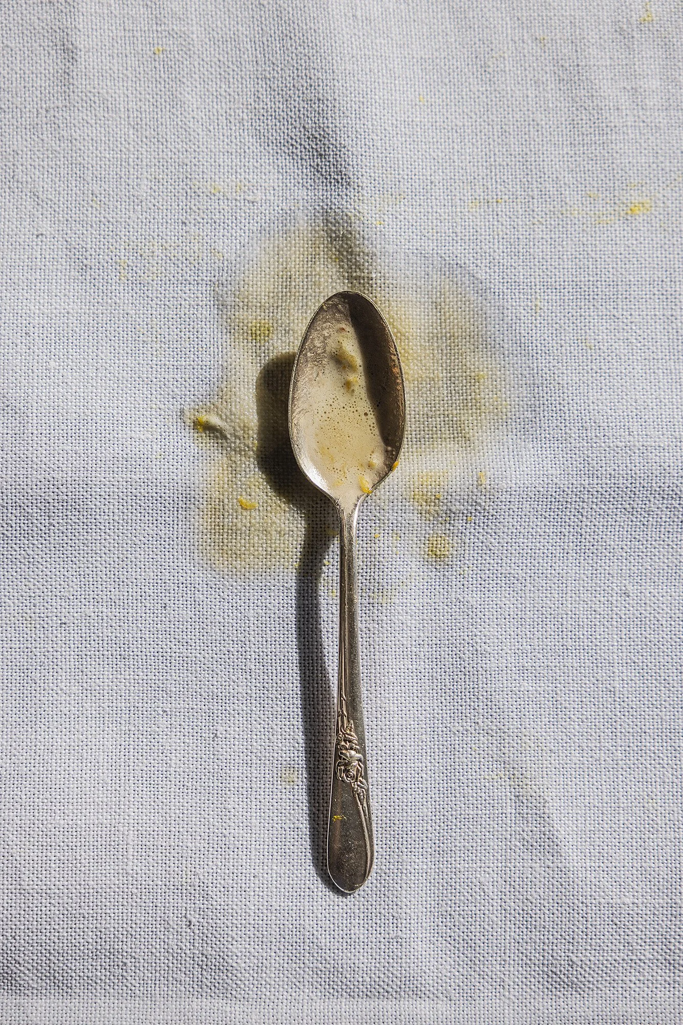A used silver spoon with lemon juice and pulp spilled around it on a white textured surface.
