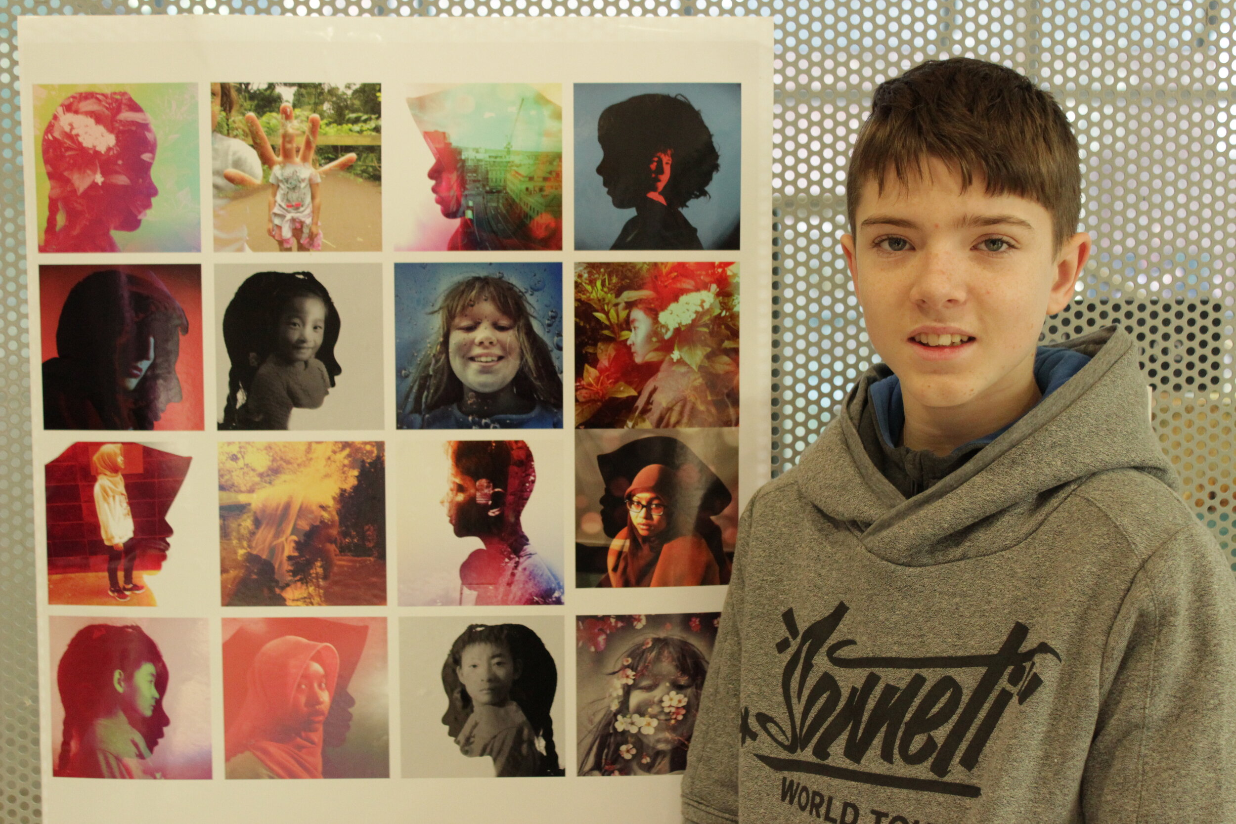 Young boy standing beside the images he has taken while they are displayed at a gallery