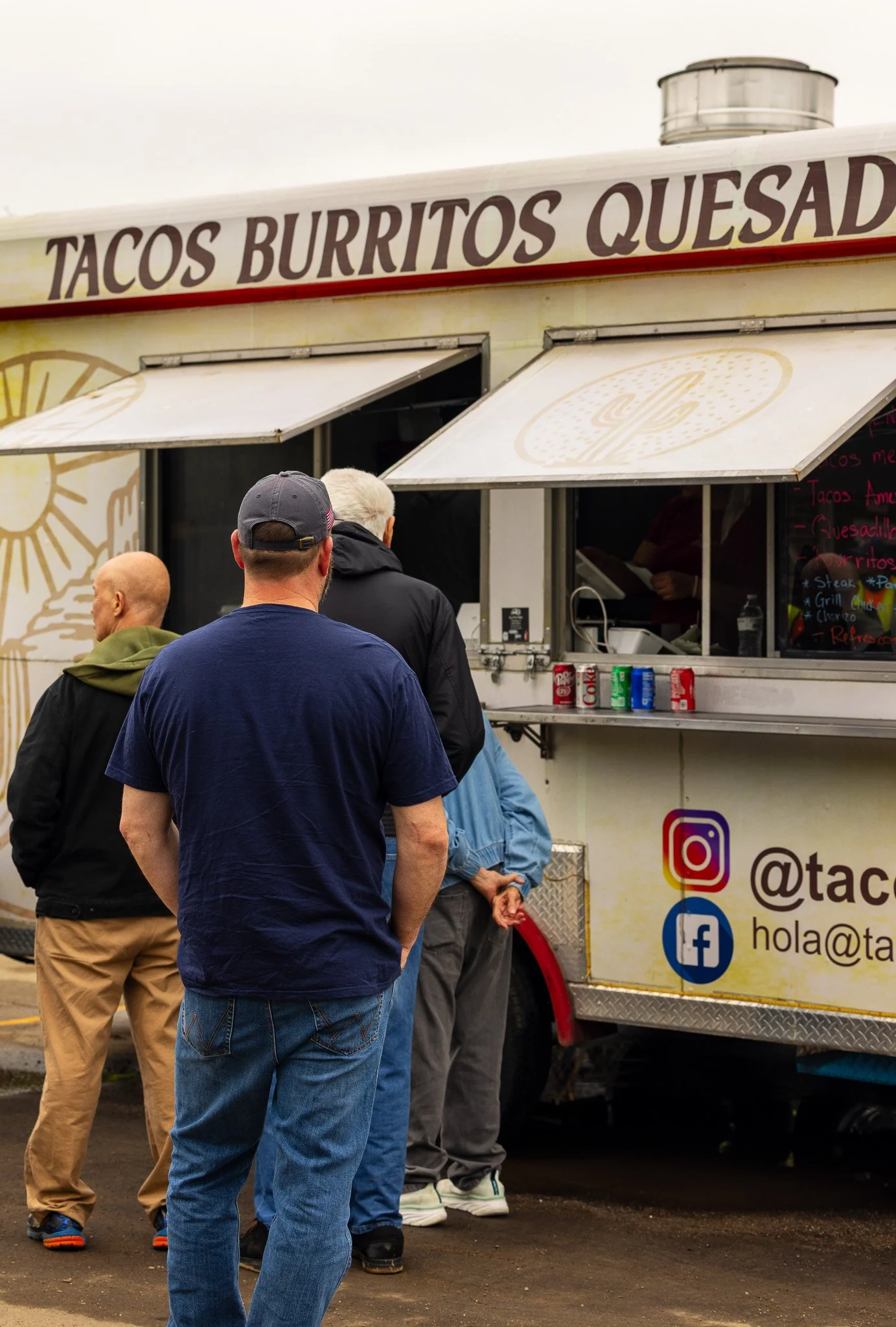 People standing in line at a food truck offering tacos, burritos, and quesadillas, with social media icons on the side.