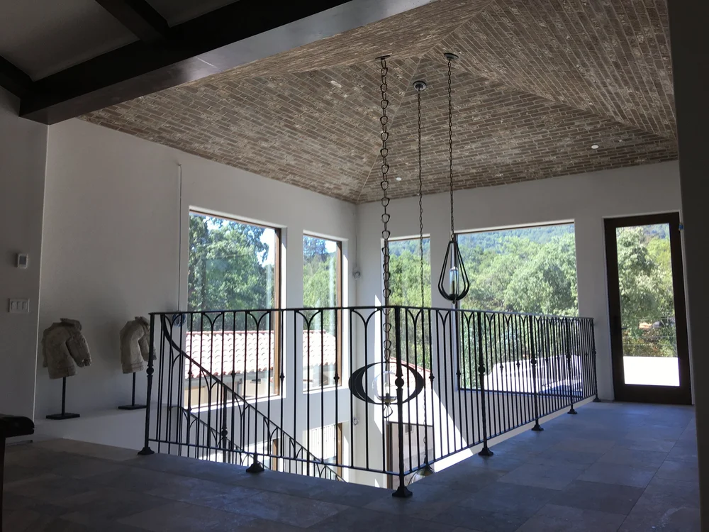  The vaulted ceiling in the entryway is sheathed with brick like an old spanish villa and is home to three artisan-created steel lighting pendants. A custom designed wrought iron railing wraps around the stairwell and bridge to the exterior roof deck